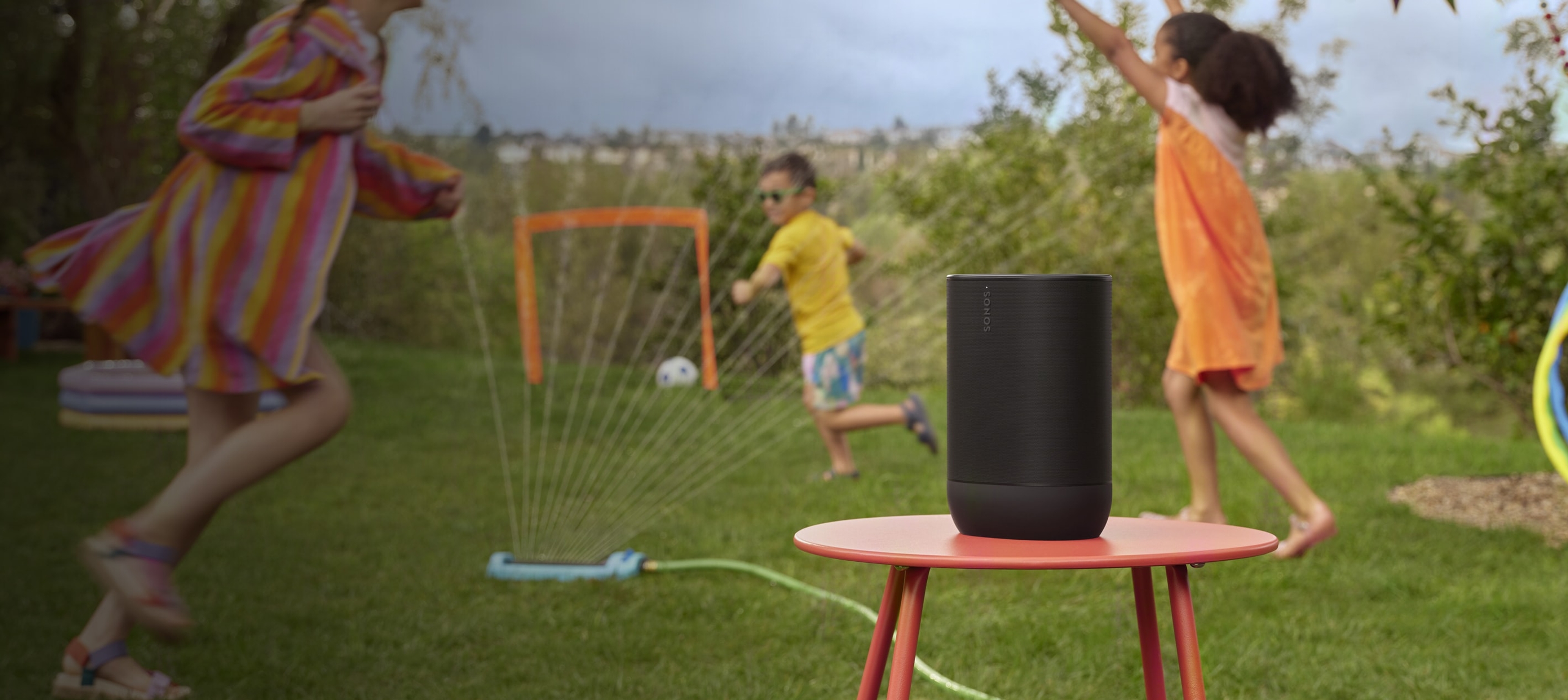 A pair of black Roam 2 portable speakers on a table with plates of food at a summer party