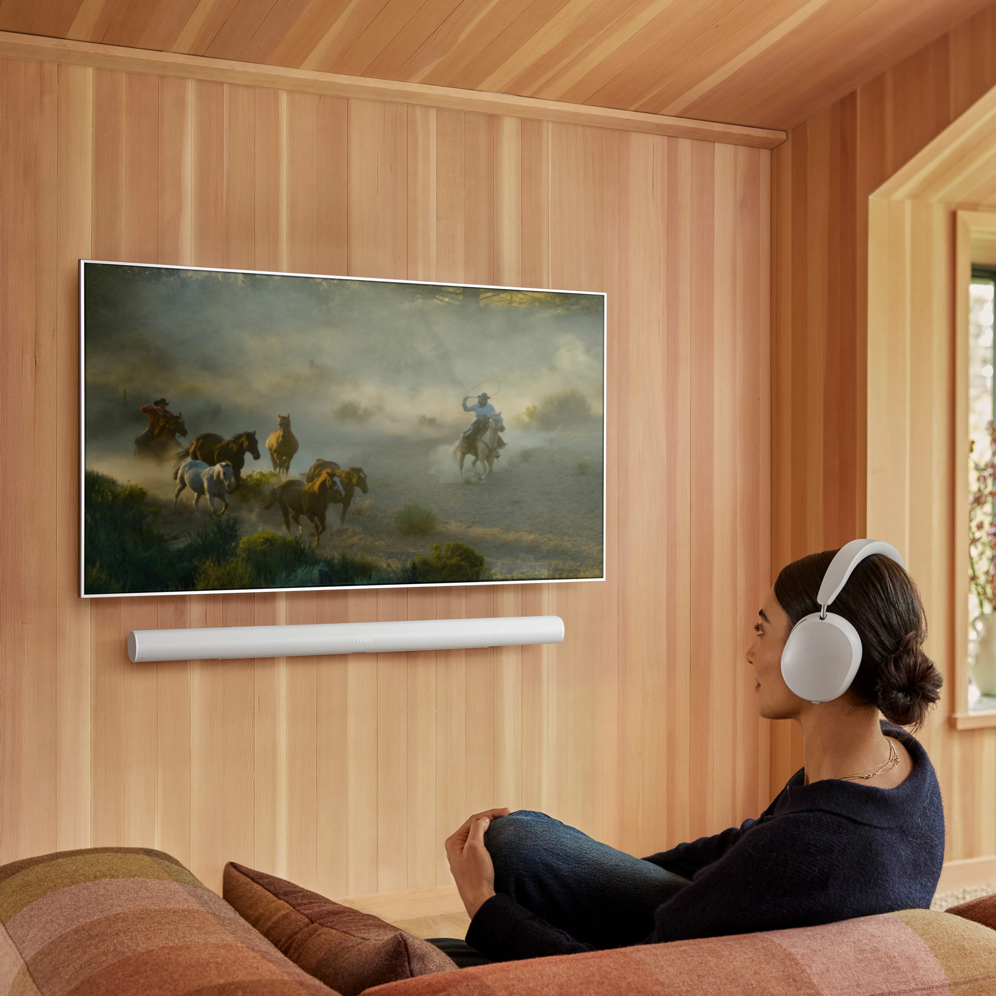 A female user on a couch using the audio swap functionality from a white Arc Ultra to her Sonos Ace headphones