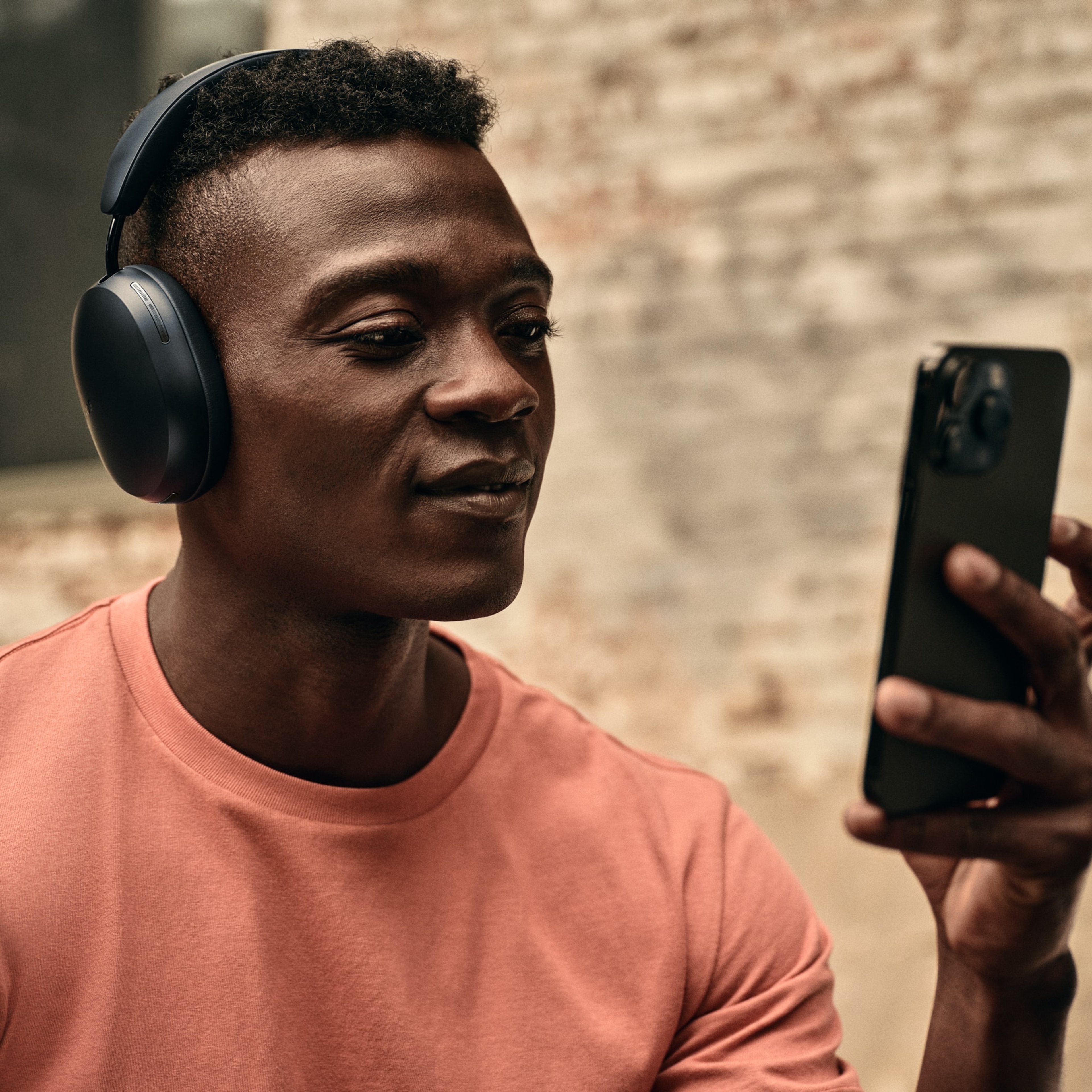 男性用户拿着手机，戴着一副黑色Sonos Ace耳机在听着什么