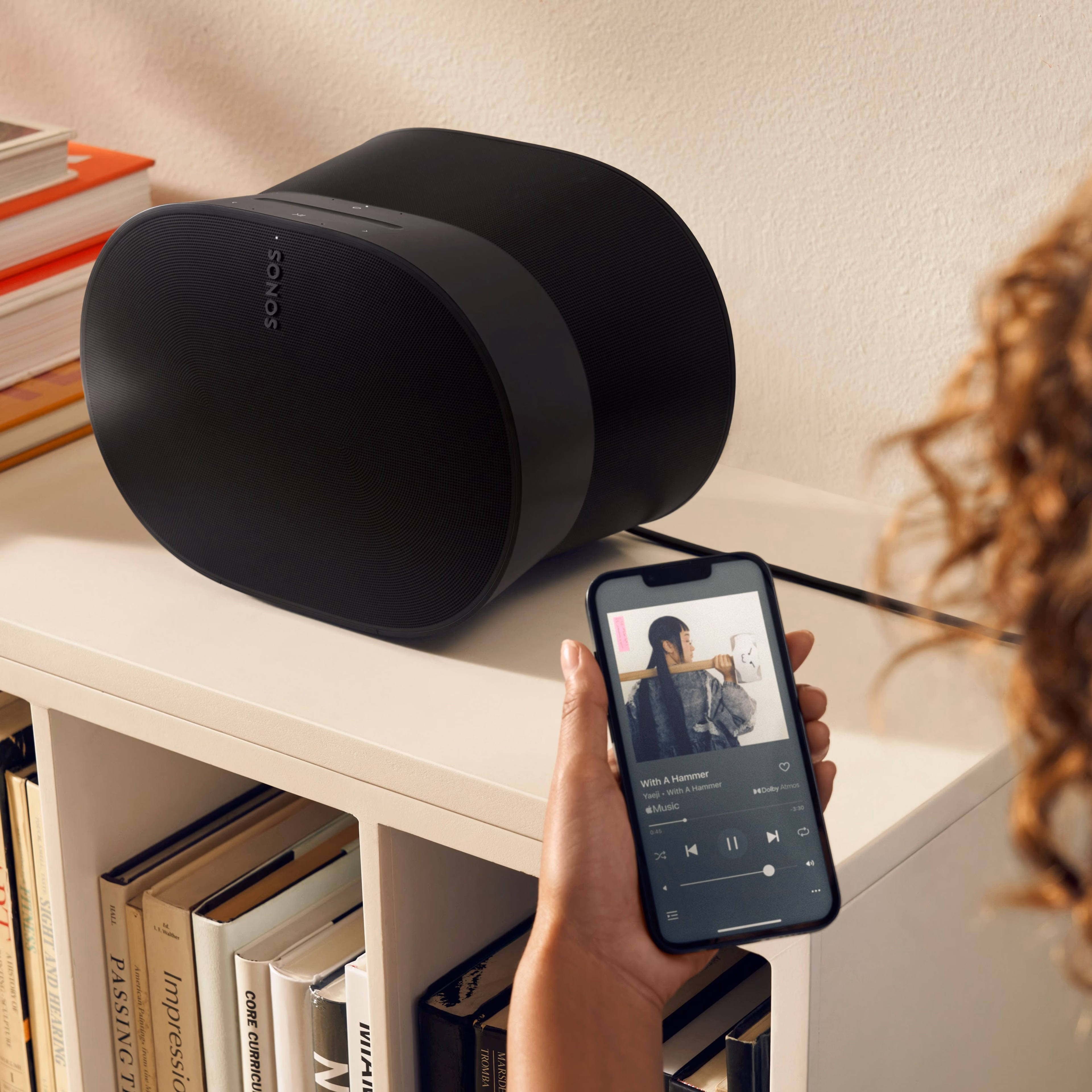 Woman using her phone to control a black Era 300 on a bookshelf