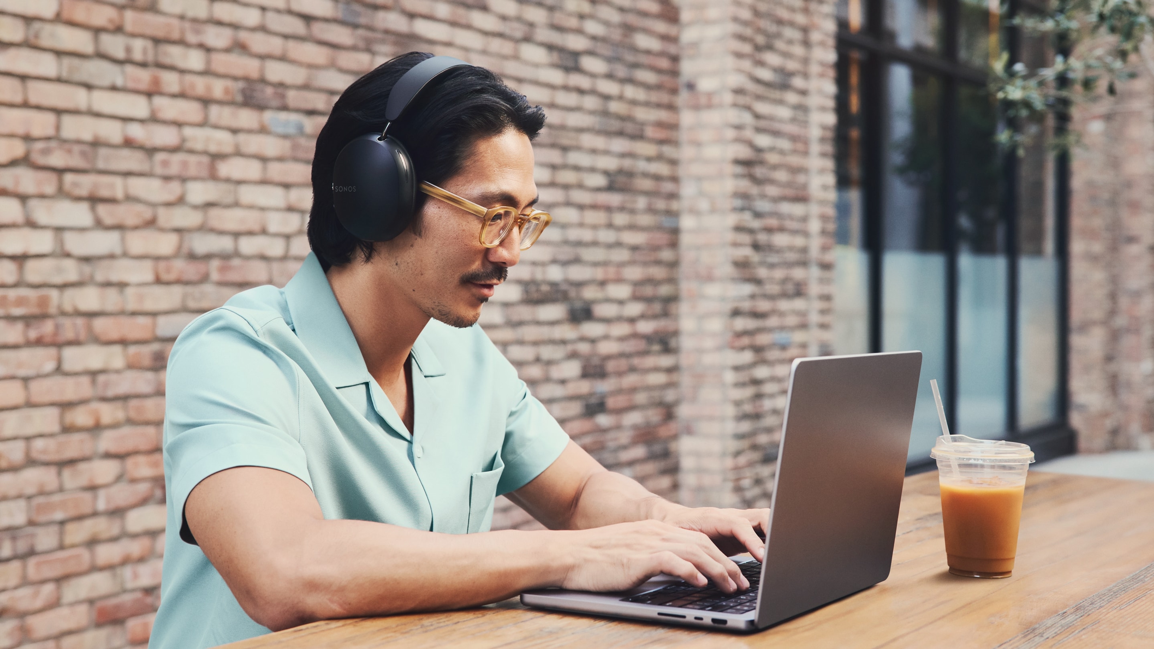 Person outdoors at a cafe and using a black Sonos Ace while on a laptop