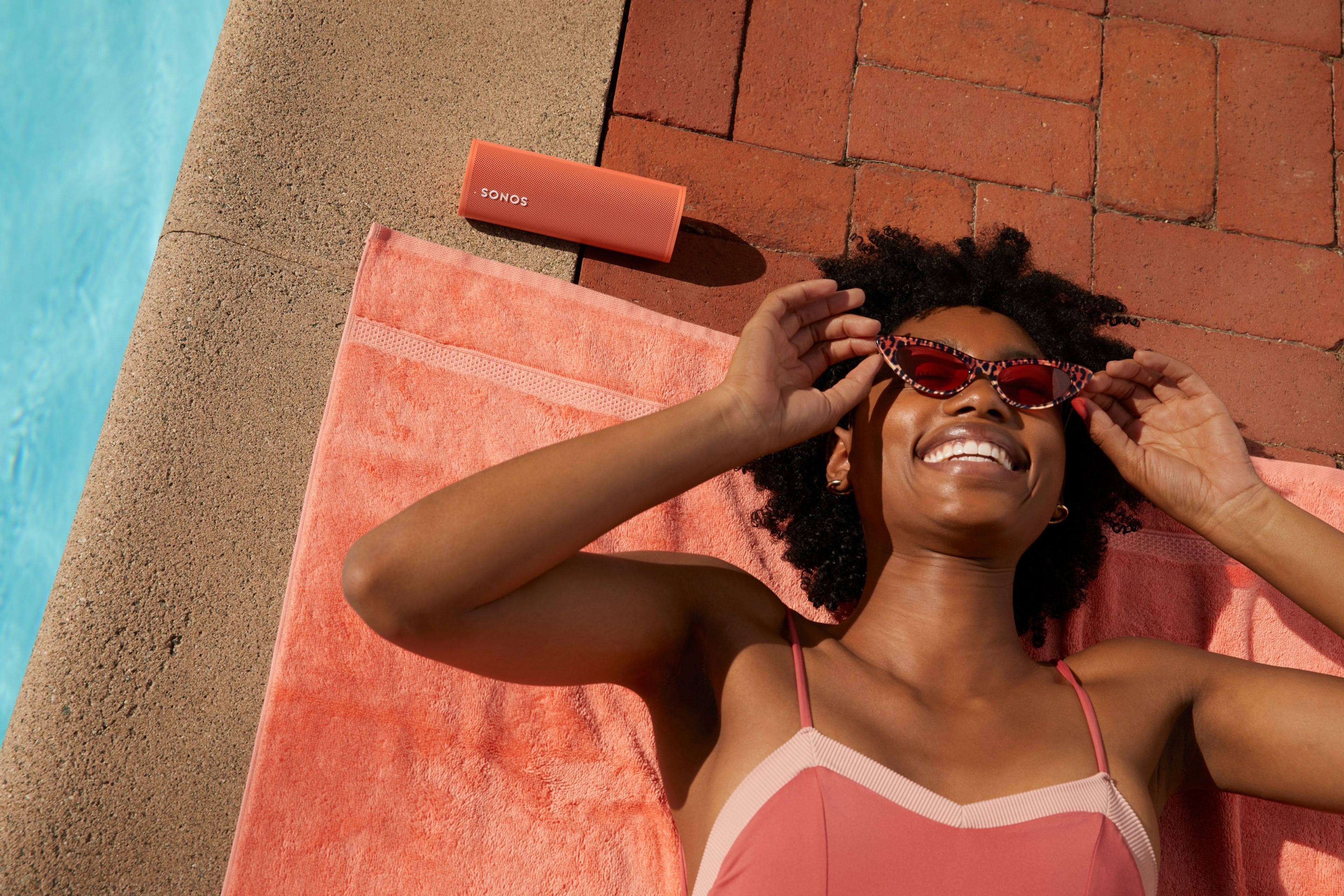 Woman laying next to pool listening to Roam speaker in Sunset
