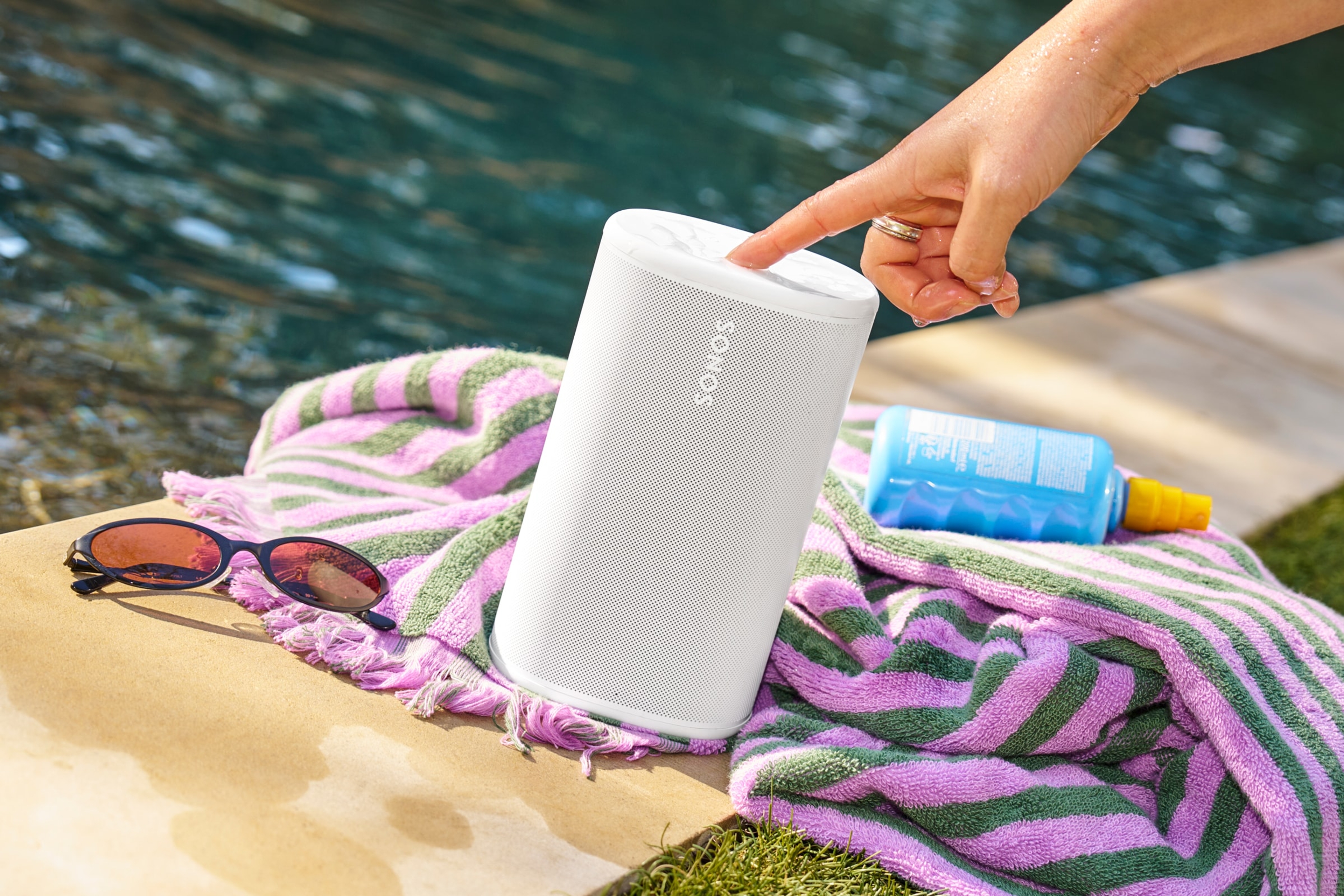 Persoană care apasă butonul de control al unei boxe Sonos Play albe de lângă piscină