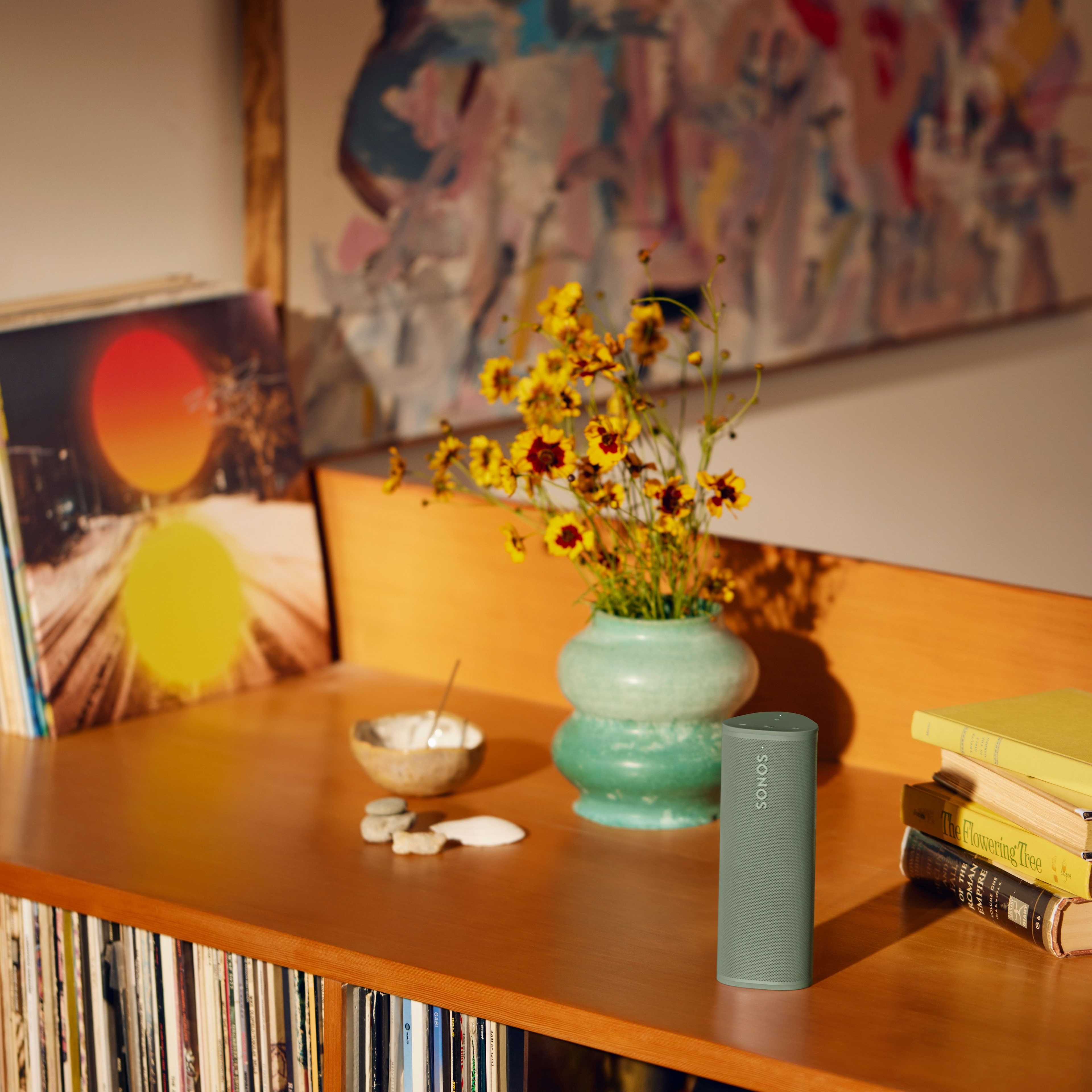 Grön Sonos Roam 2 på en hylla bredvid en vas med blommor och böcker