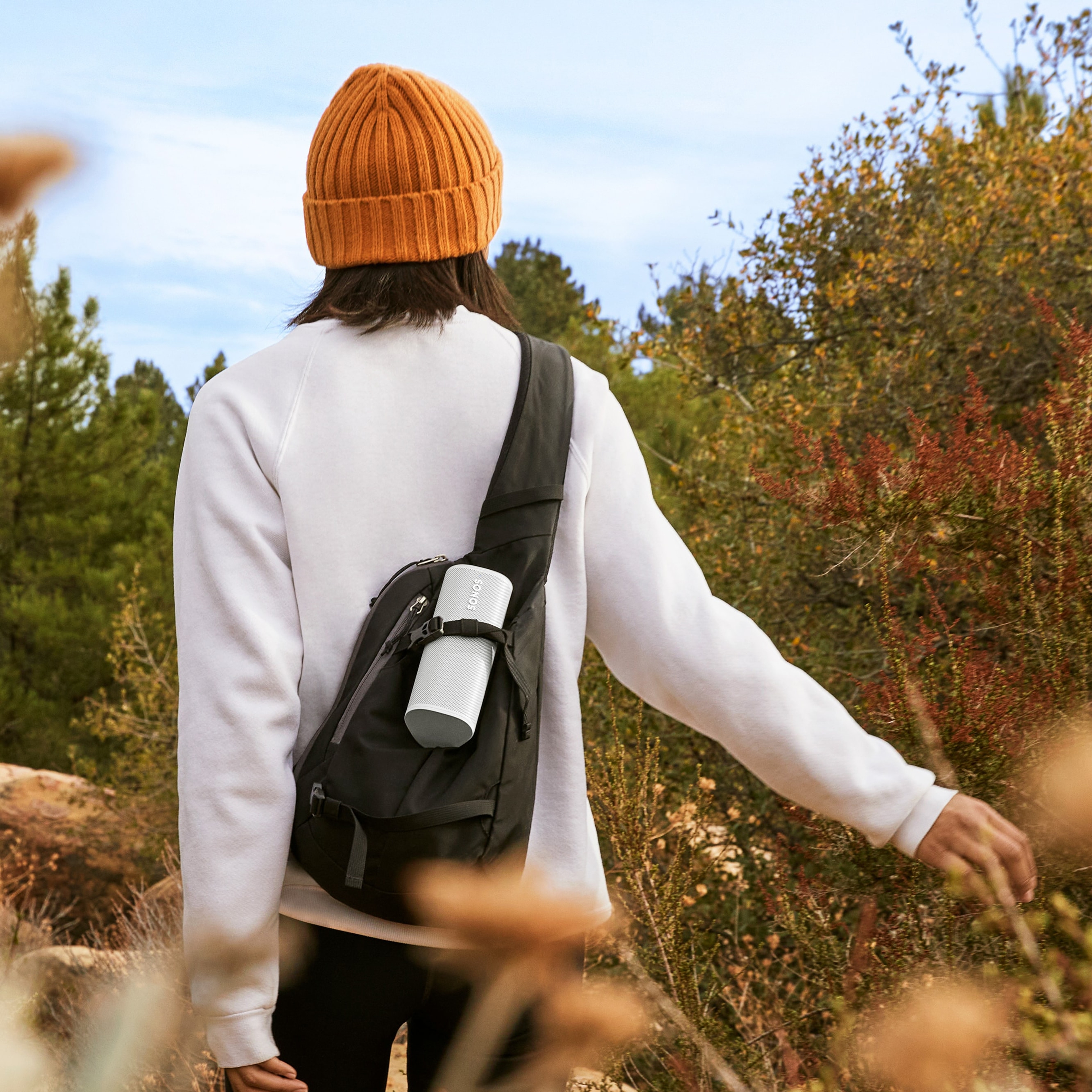 Woman hiking outdoors with a Lunar White Sonos Roam in her backpack