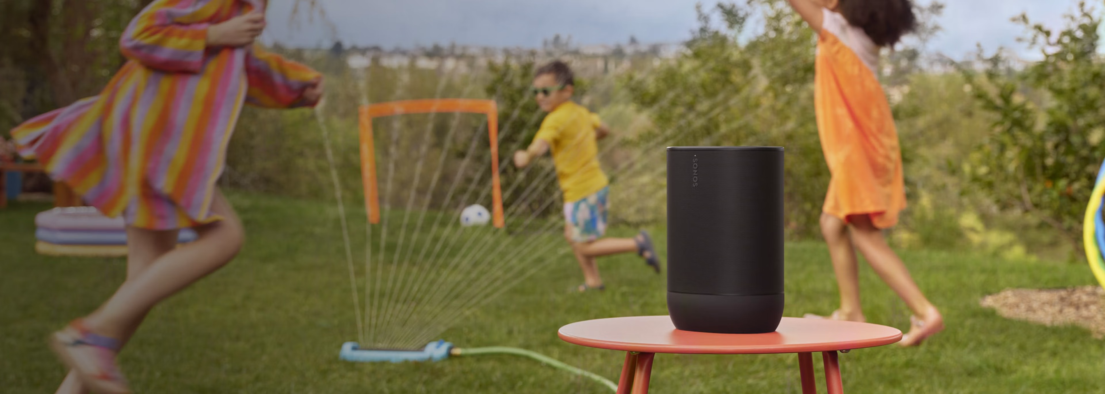 Sonos Move 2 auf einem Standfuß, mit Kindern die draußen spielen