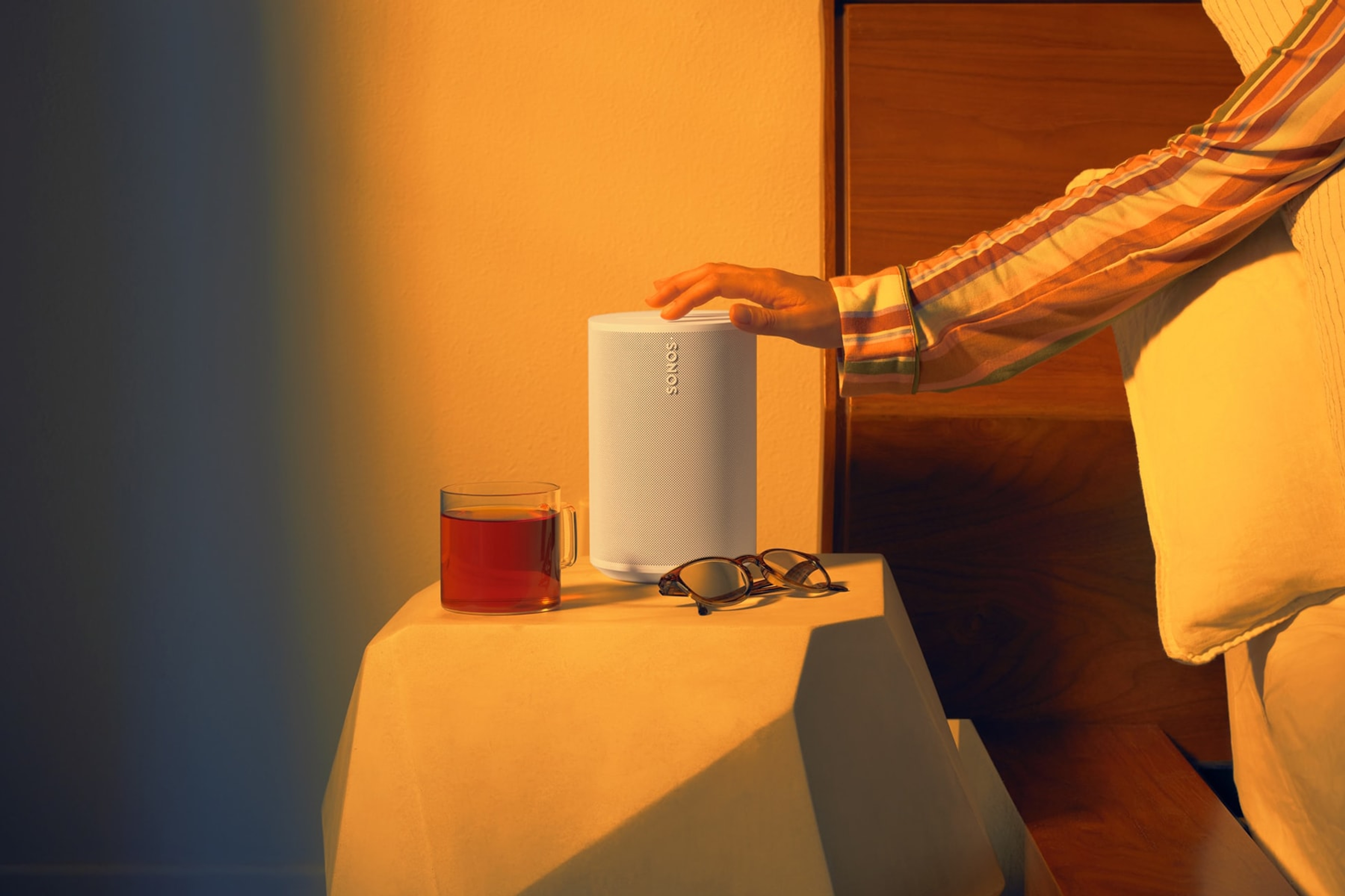 Un utilisateur se servant des commandes tactiles d'une enceinte Sonos Era 100 blanche près de son lit