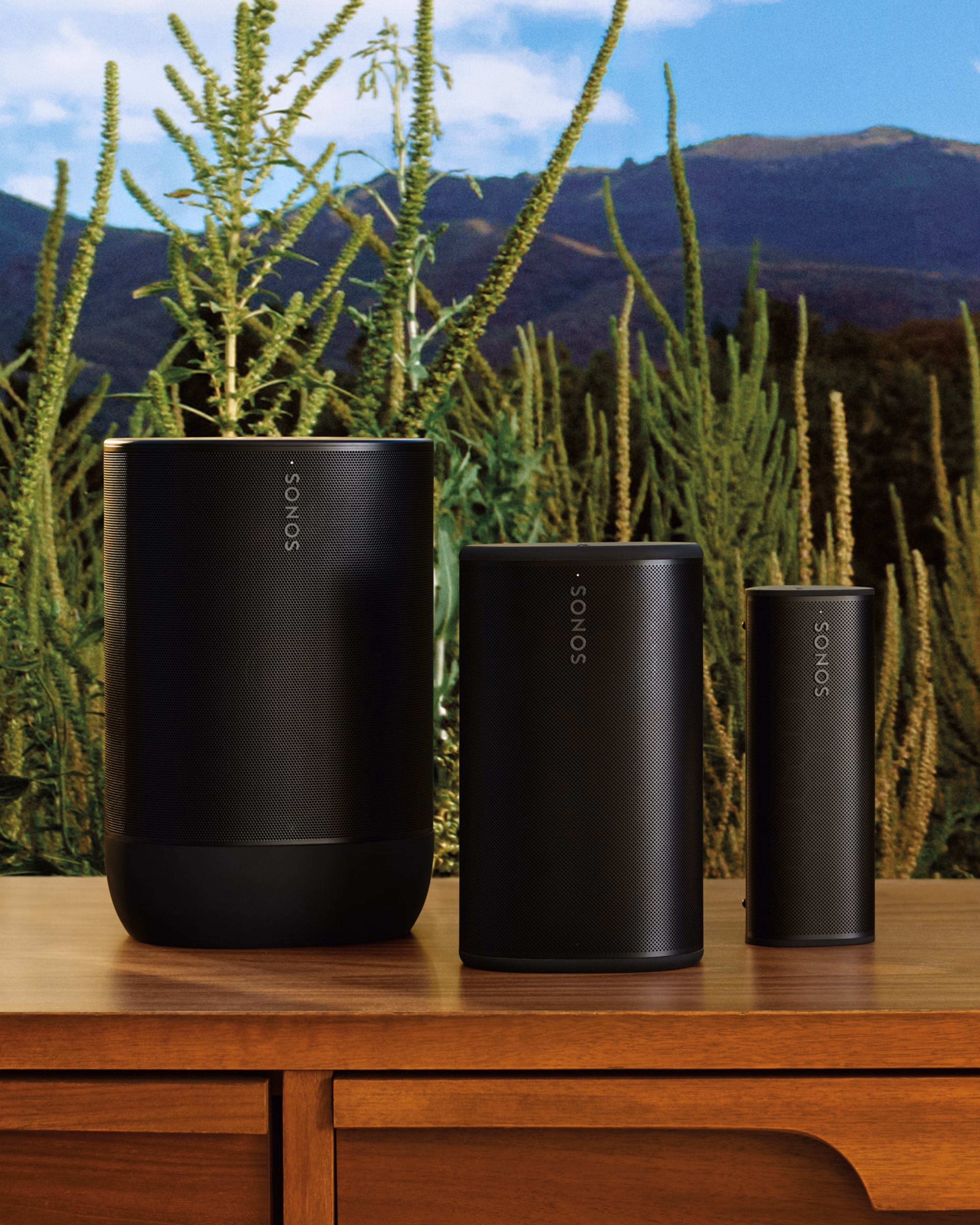 屋外のテーブルの上に並べて置いてあるブラックのSonosポータブルスピーカー - Sonos Move 2、Sonos Play、Sonos Roam 2