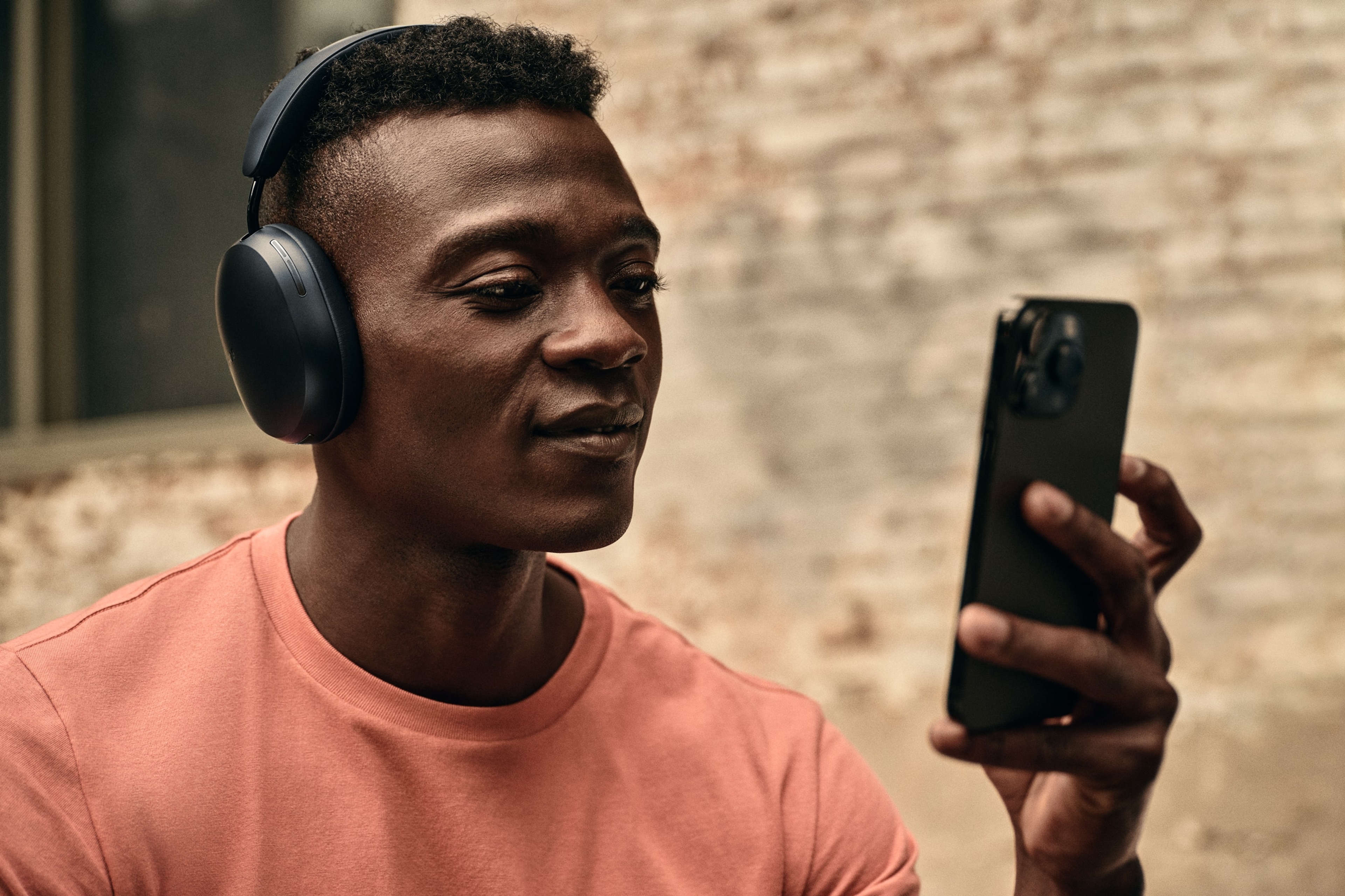 Male user with phone while listening on a pair of black Sonos Ace headphones