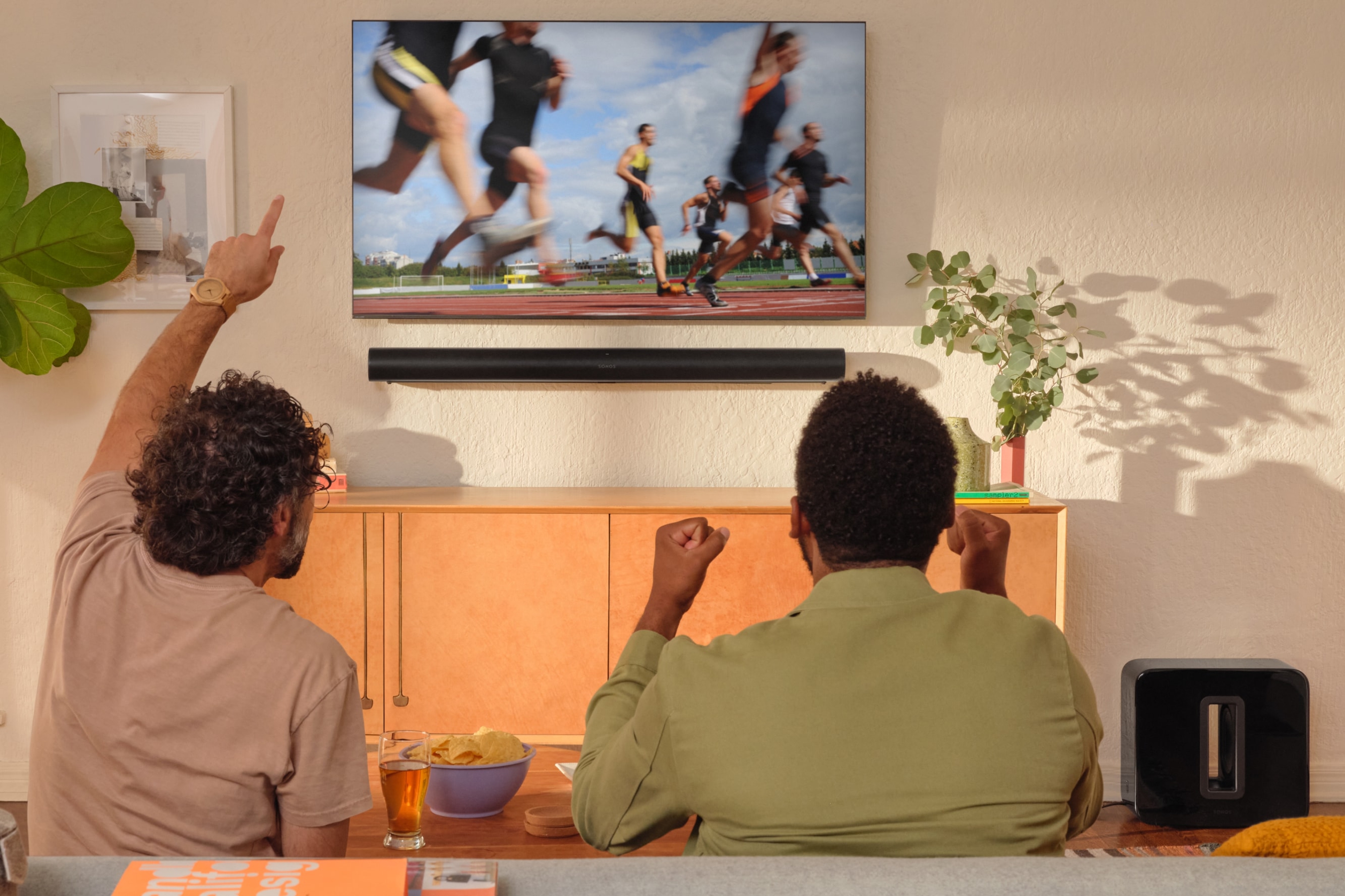 Deux personnes regardent l'athlétisme à la TV avec Sonos Arc et Sub noirs