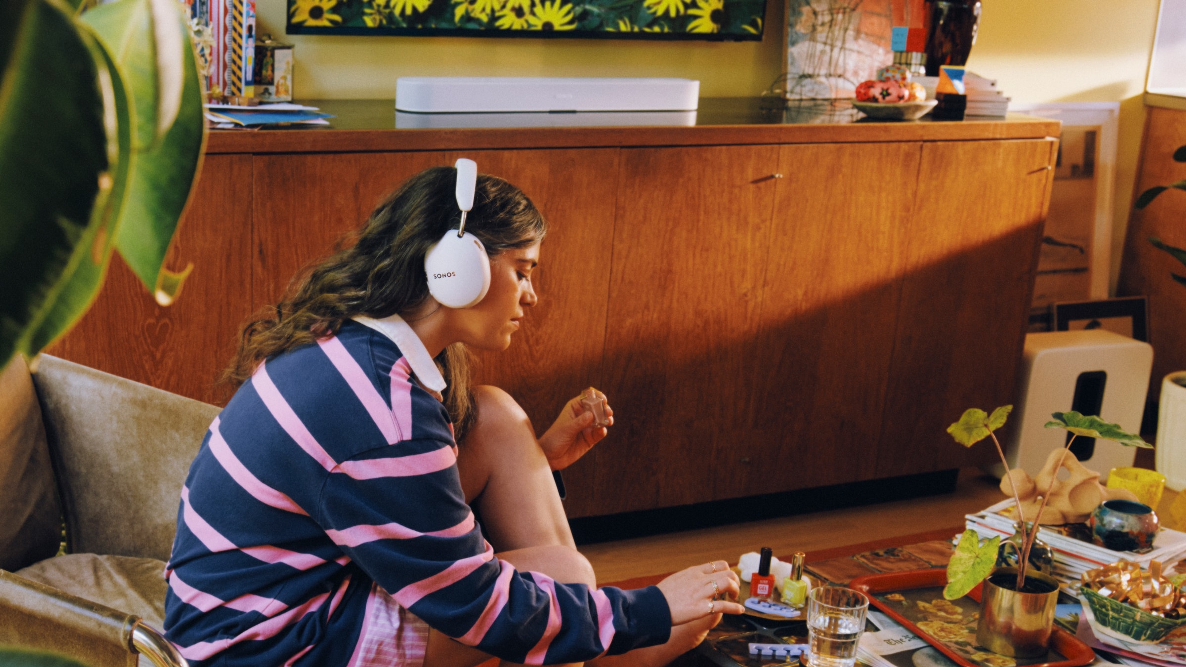 Person wearing a white Sonos Ace Ultra headphones with a white Beam Ultra in the background