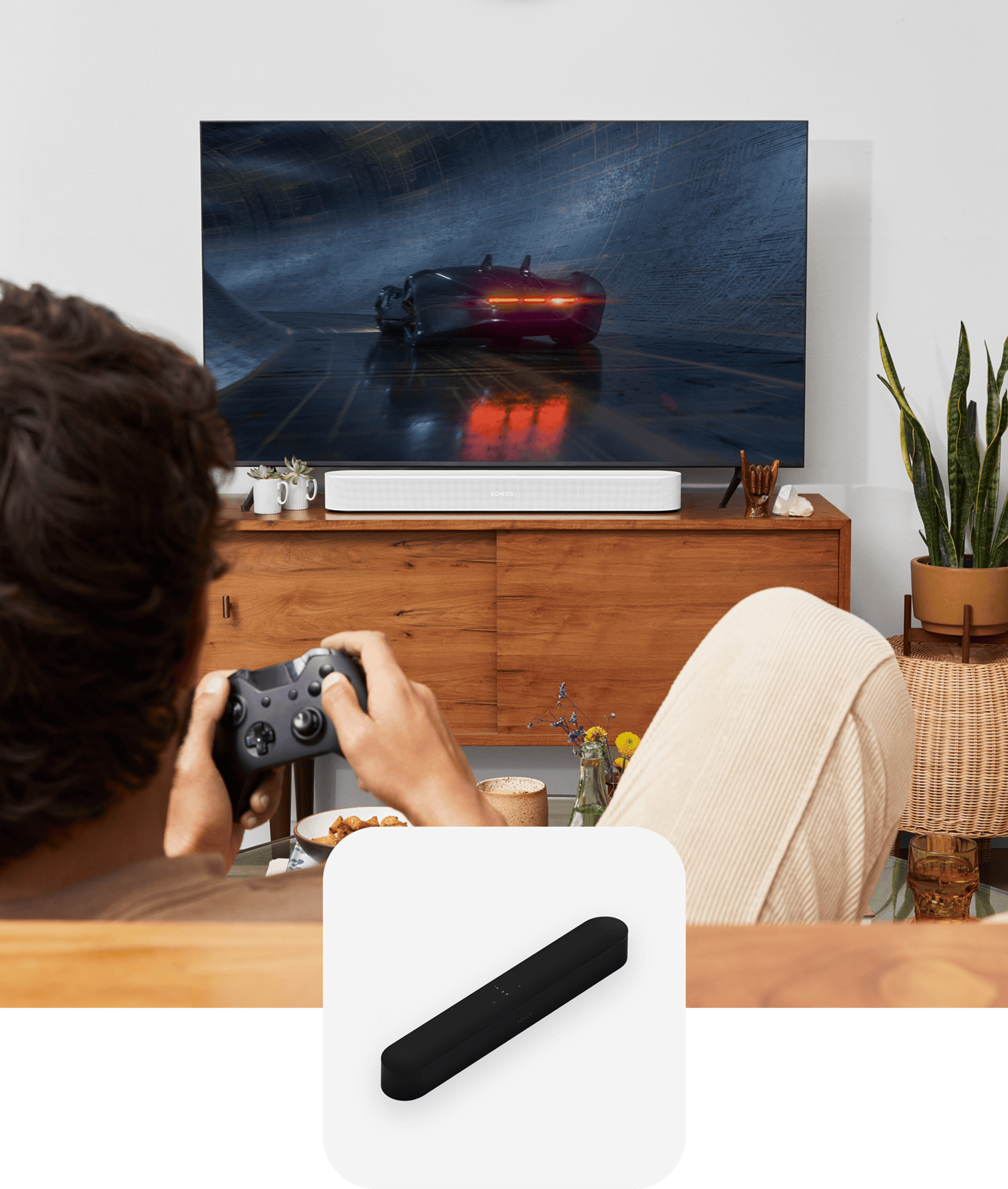 User sitting on couch gaming with a white Sonos Beam soundbar for audio