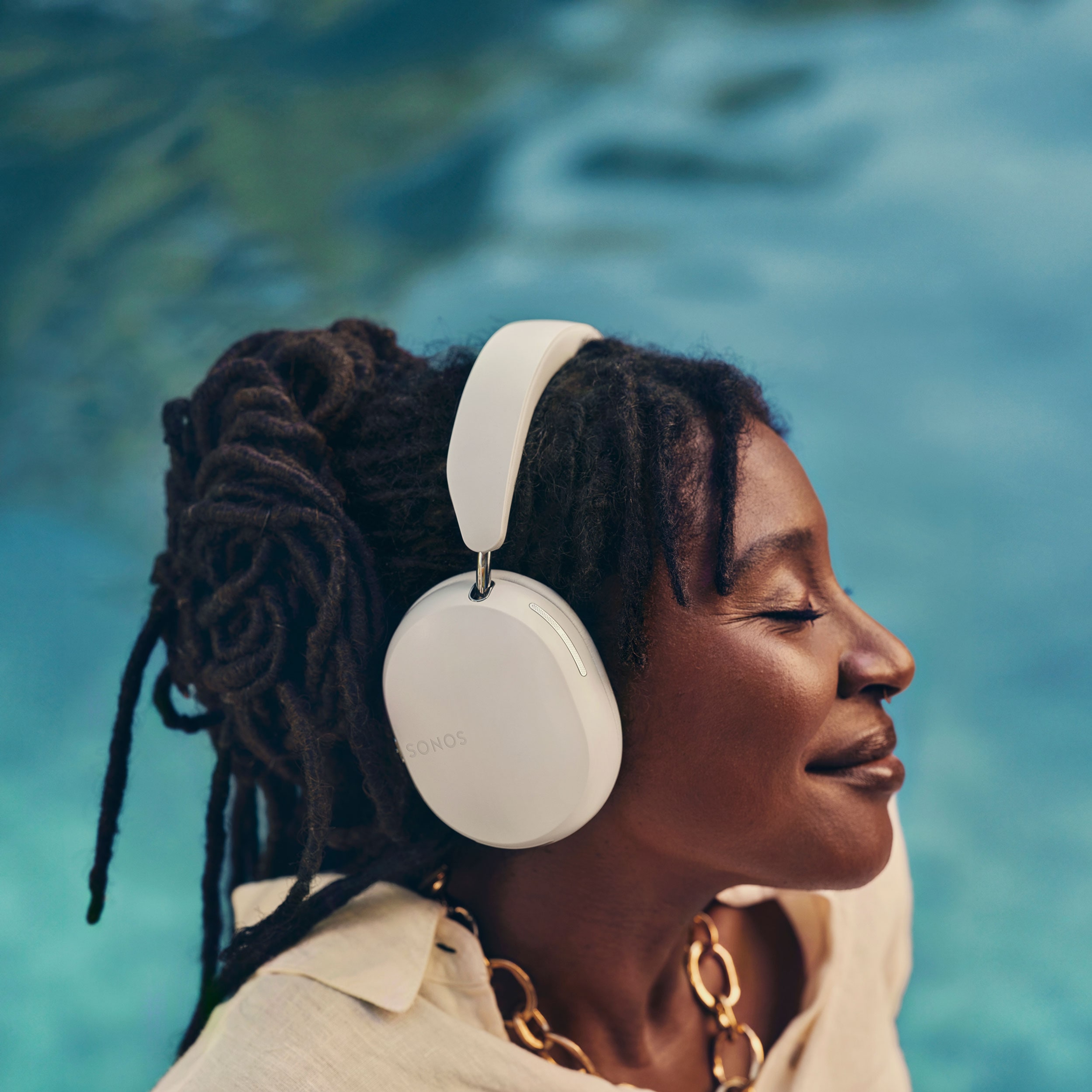 Person smiling listening to music on white Sonos Ace headphones by the pool