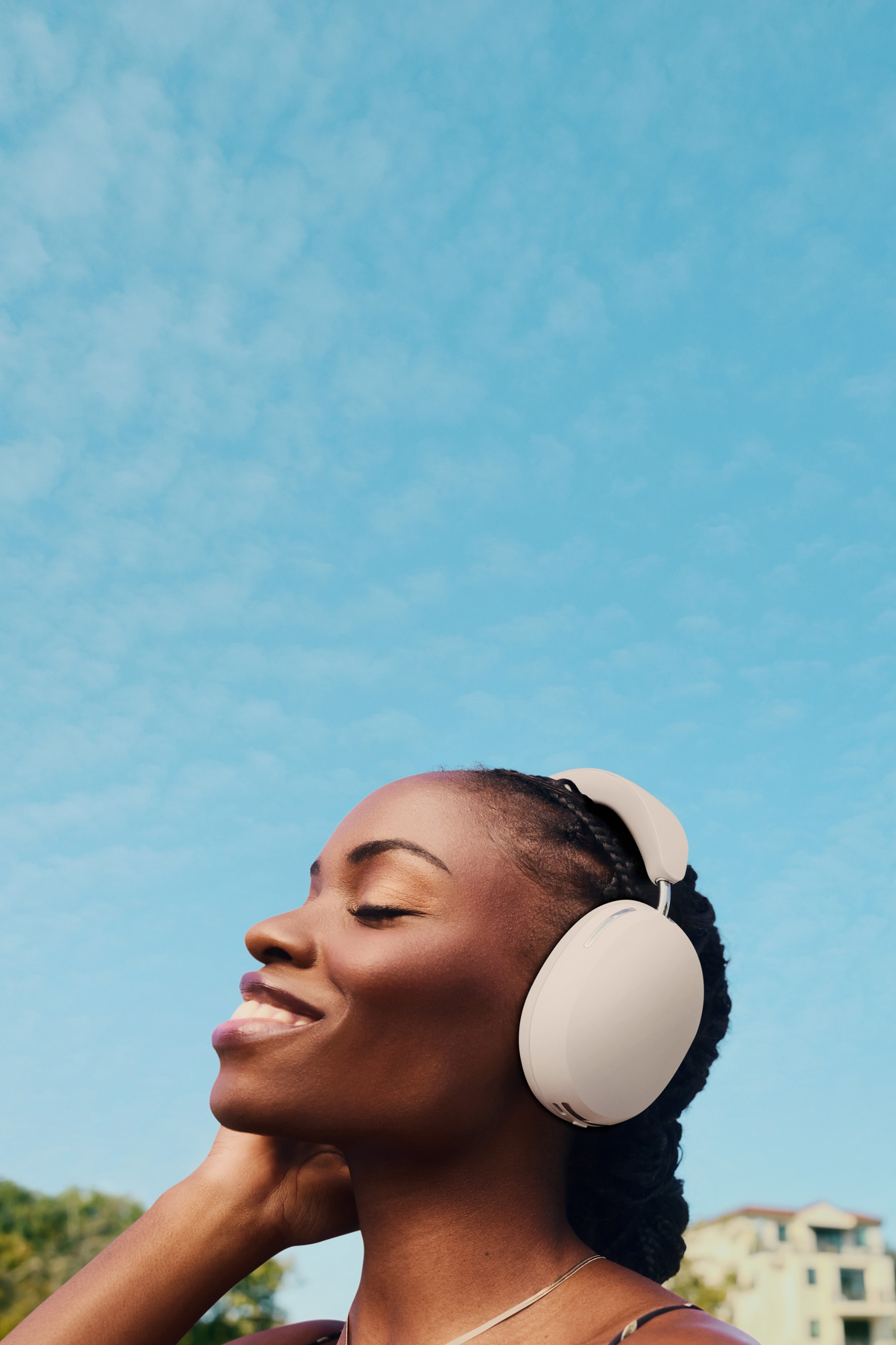 Person som lytter til musikk med Sonos Ace-hodetelefoner, utendørs med himmel i bakgrunnen