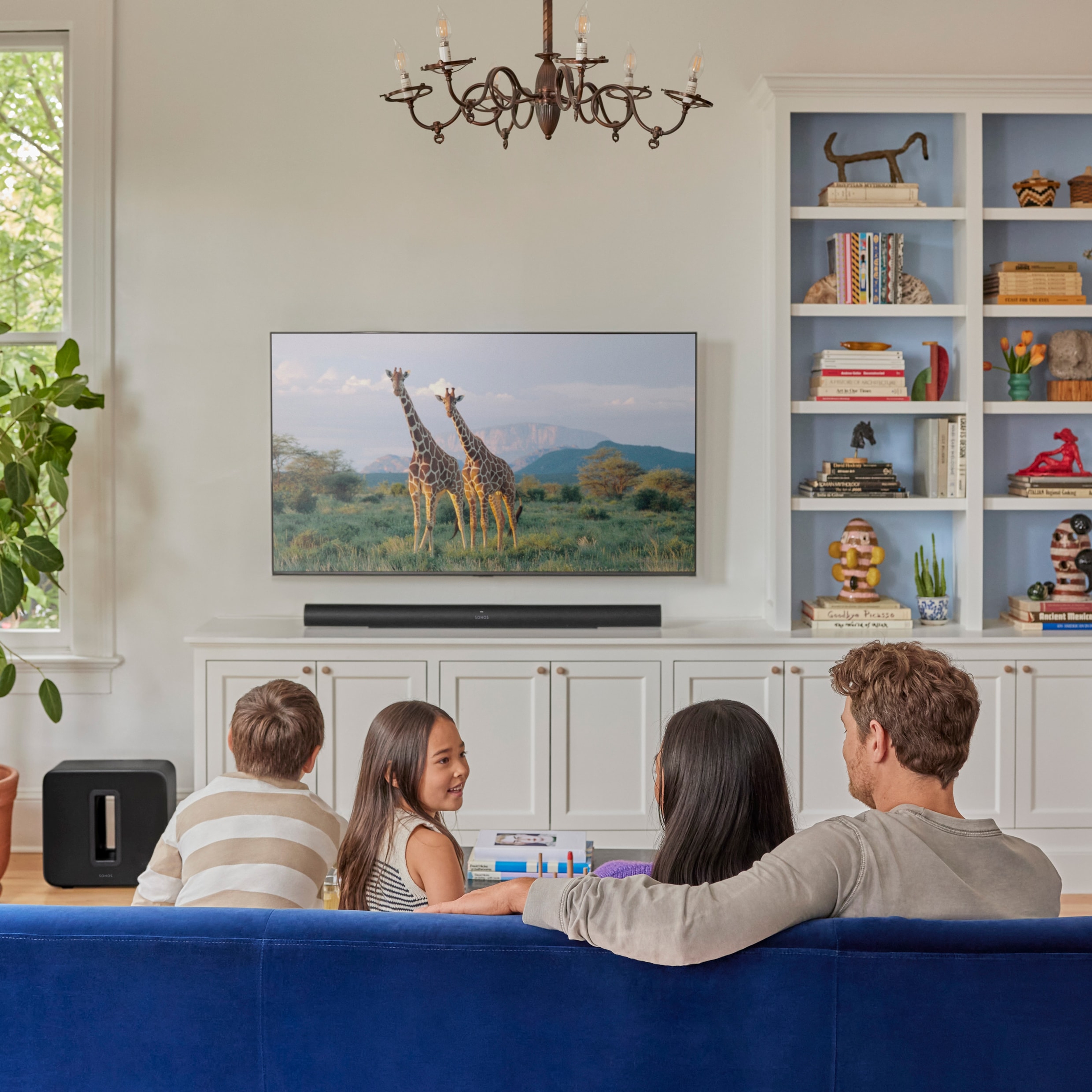 Famille assise dans le salon regardant la télévision avec un Arc Ultra noir et un Sub 4 noir