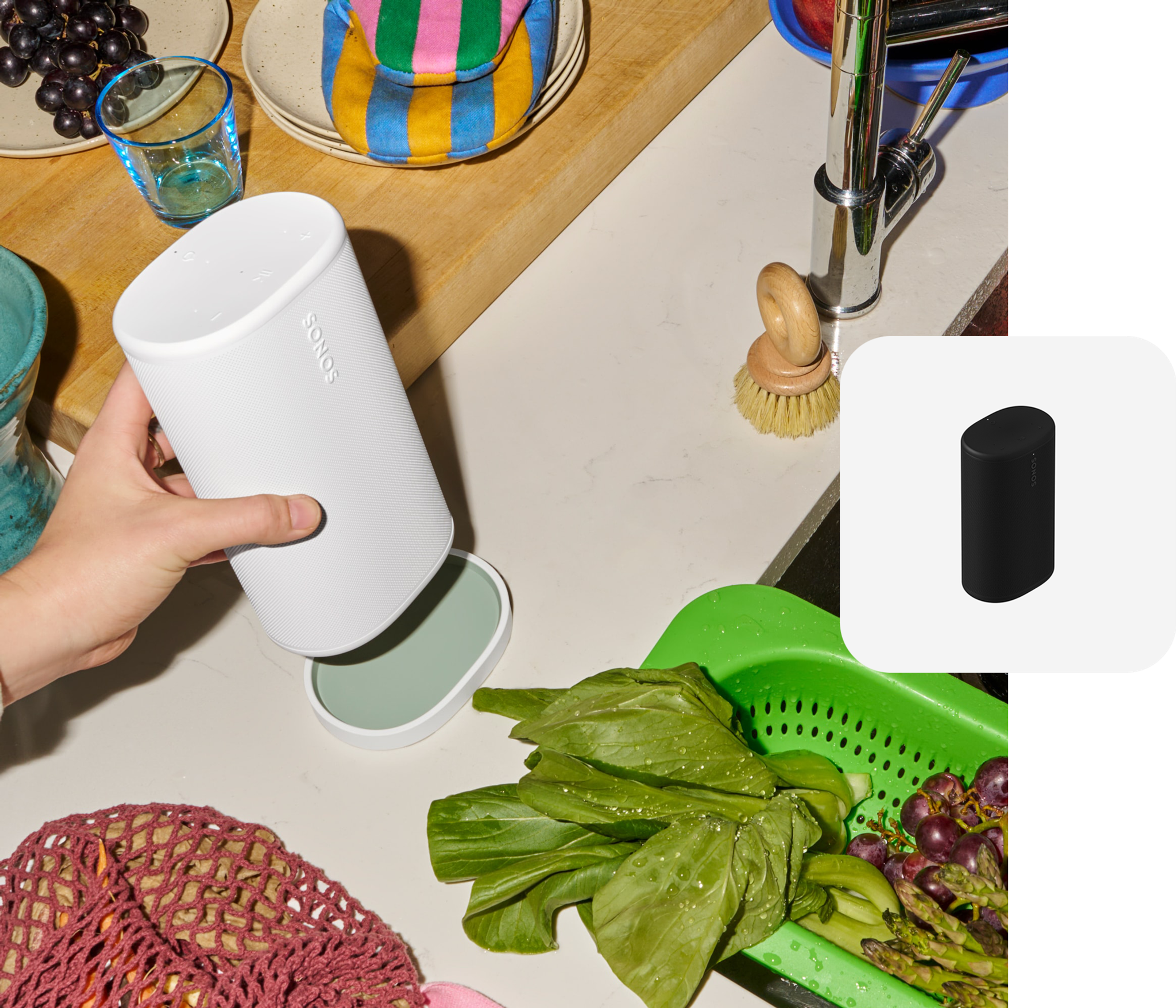 Hand placing a white Sonos Play on the charging base next to a kitchen sink