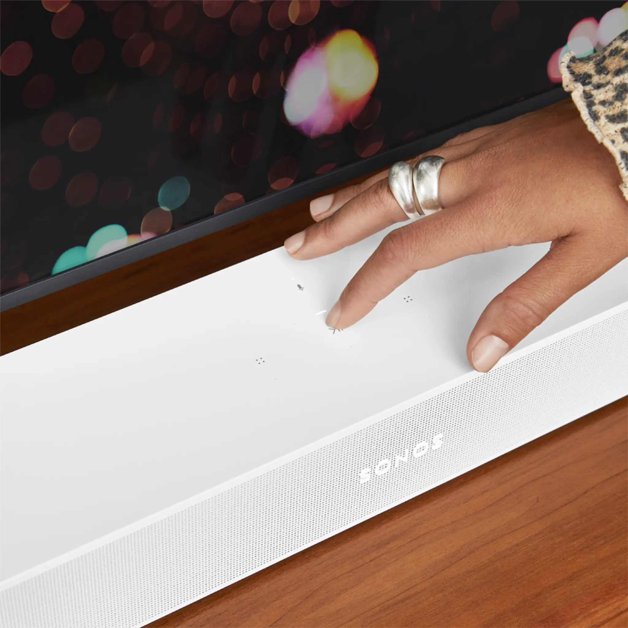 A person's hand touching the Play/Pause button on Sonos Beam