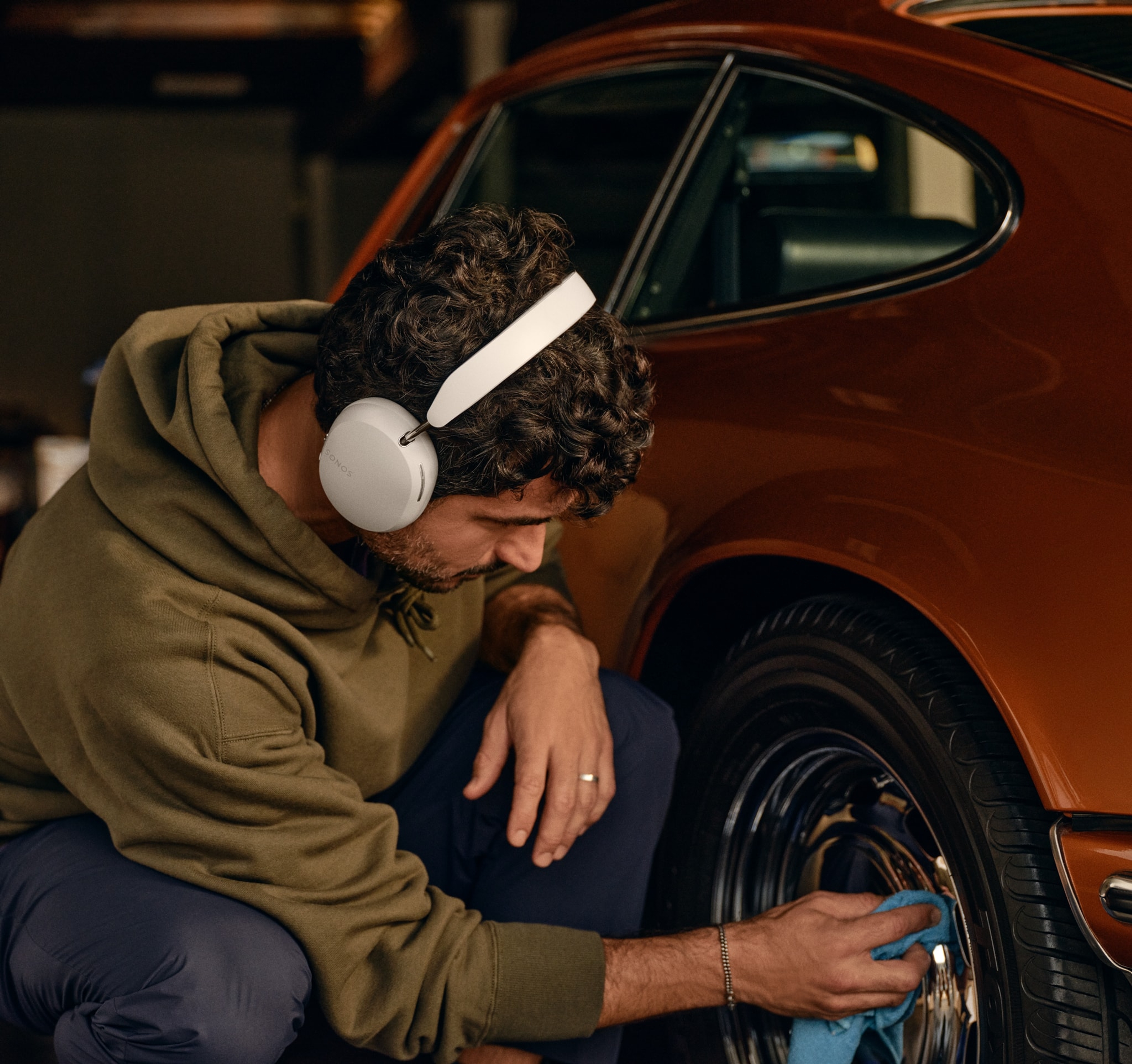 Un uomo indossa un paio di cuffie Sonos Ace nel colore Soft White mentre lucida le ruote di un’auto d’epoca