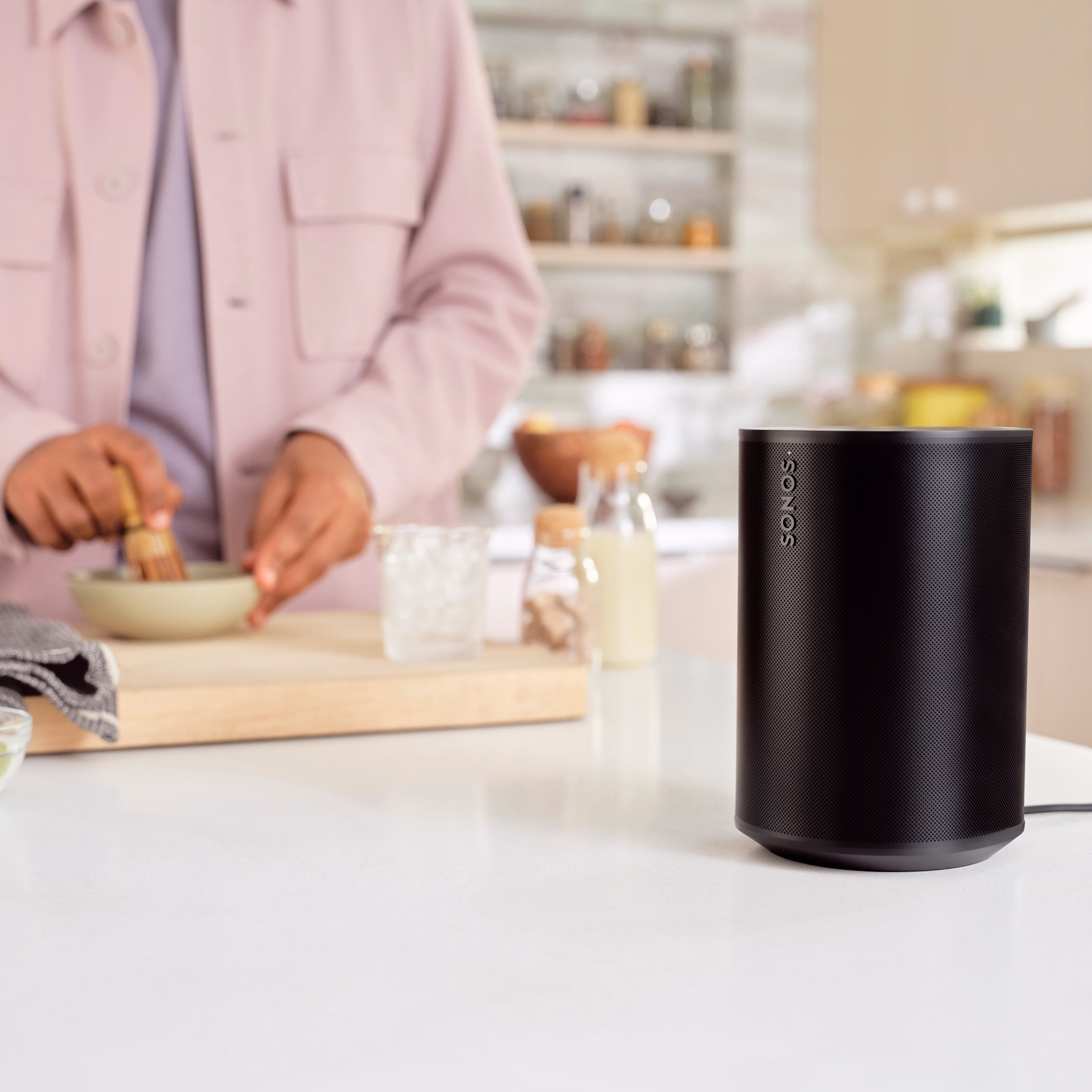 A black Era 100 speaker on a kitchen countertop next to someone preparing a drink