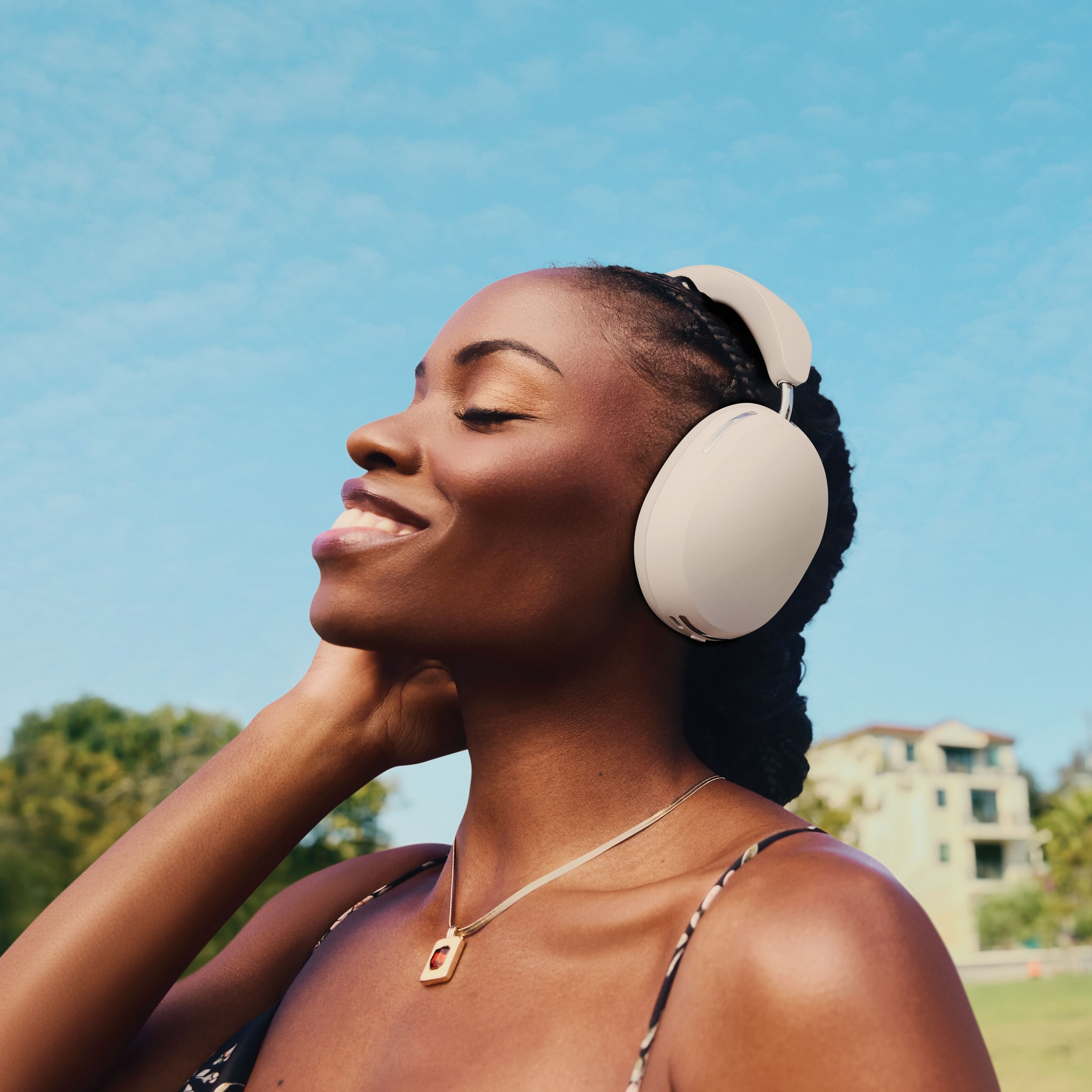 Person smiling and listening to music on Soft White Sonos Ace headphones outside