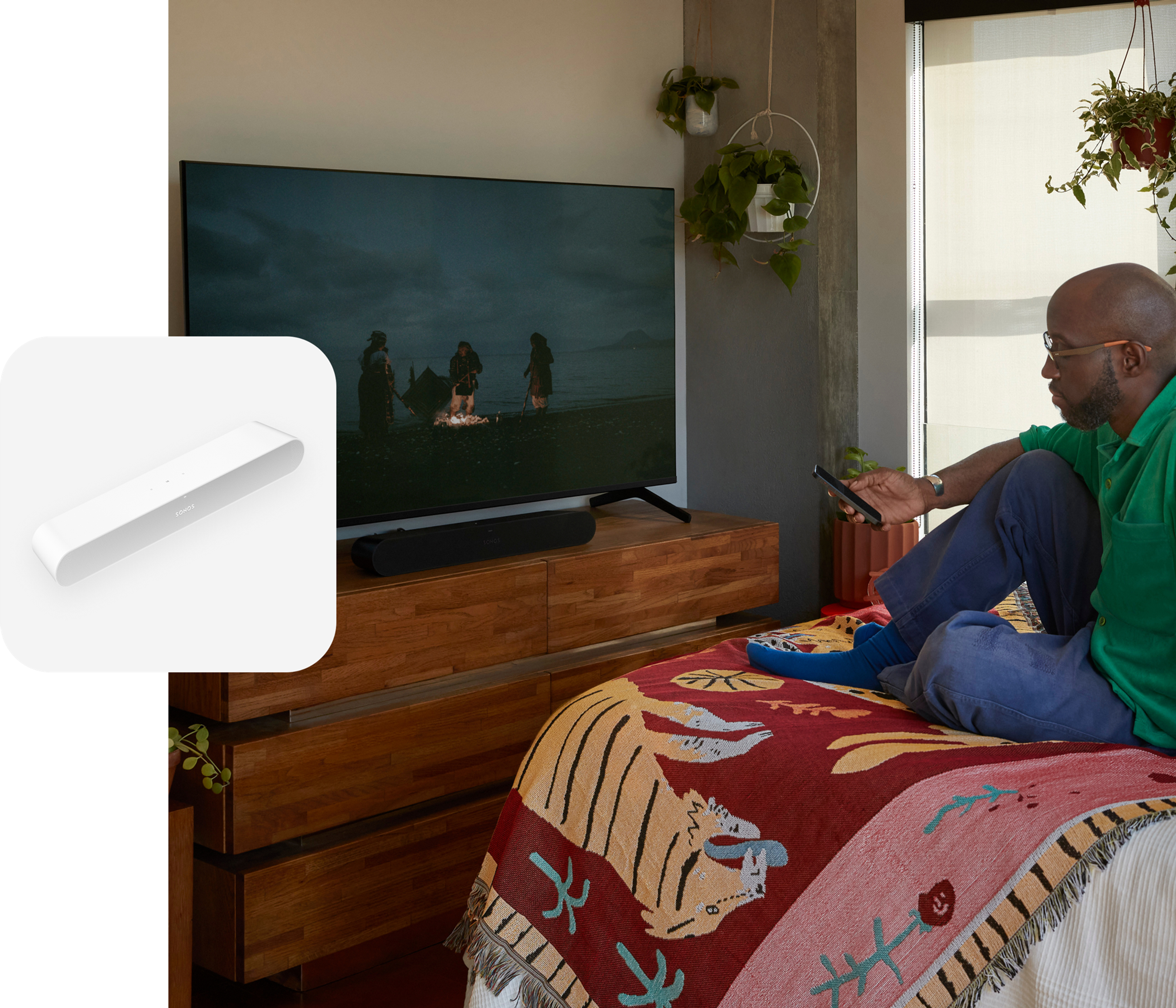 User sitting on their bed watching a movie with sound from a black Ray soundbar