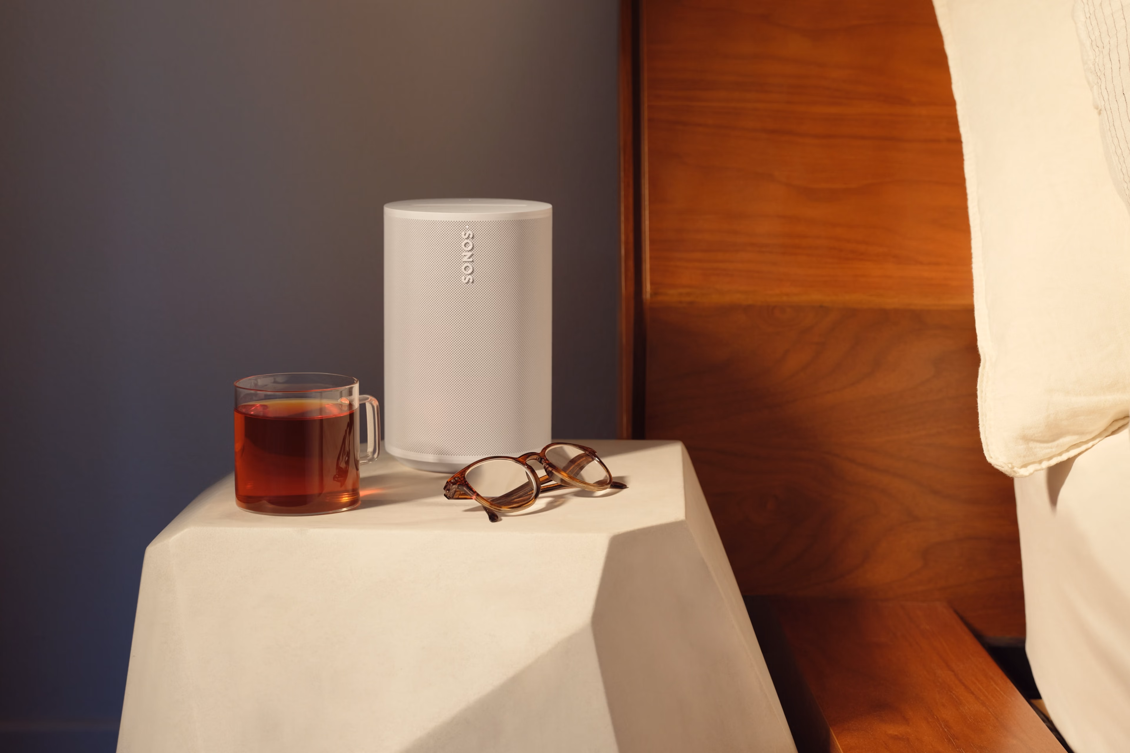 A white Era 100 speaker on a nightstand next to a bed