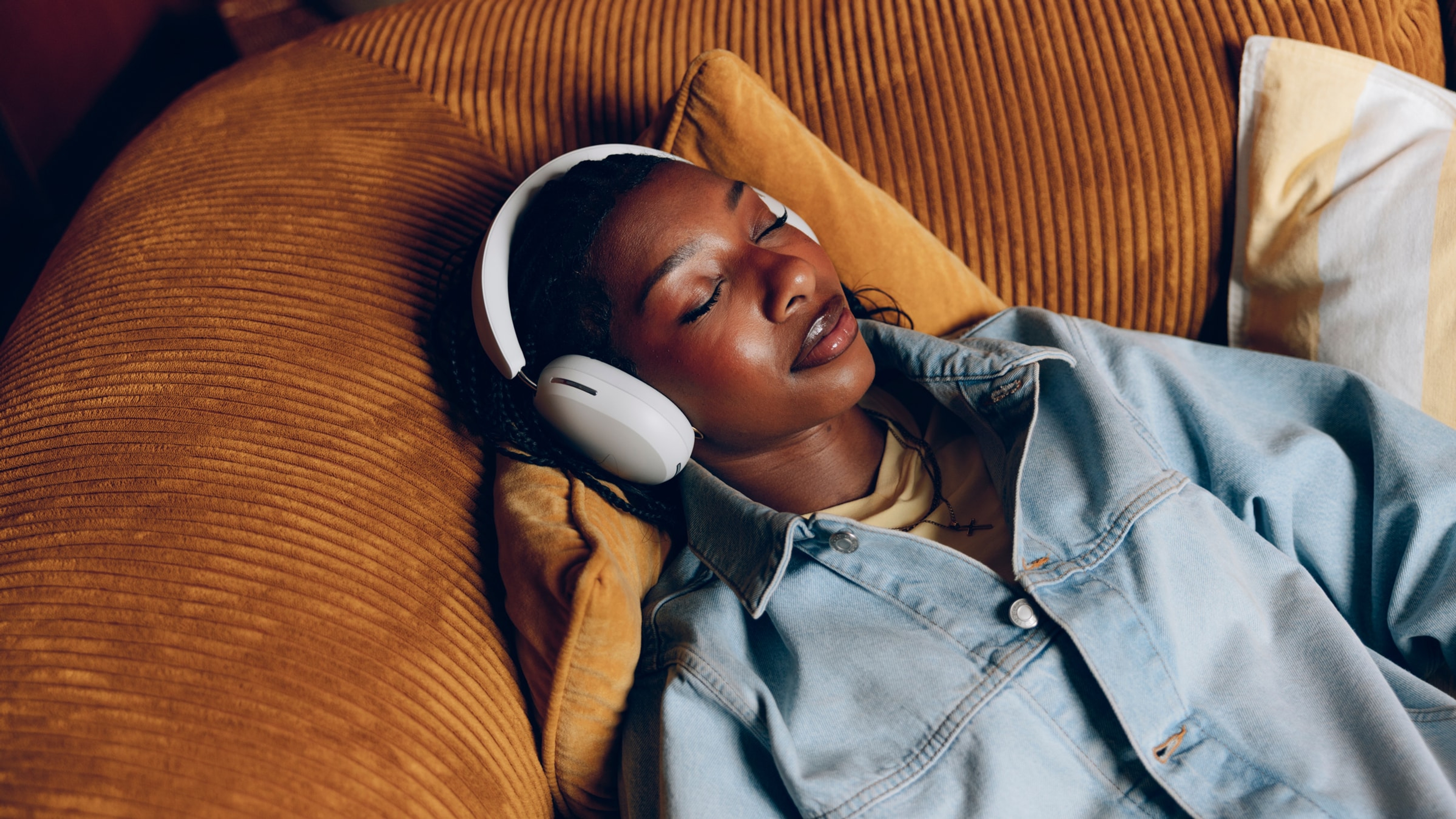 Nia Smith laying on a couch wearing Sonos Ace headphones