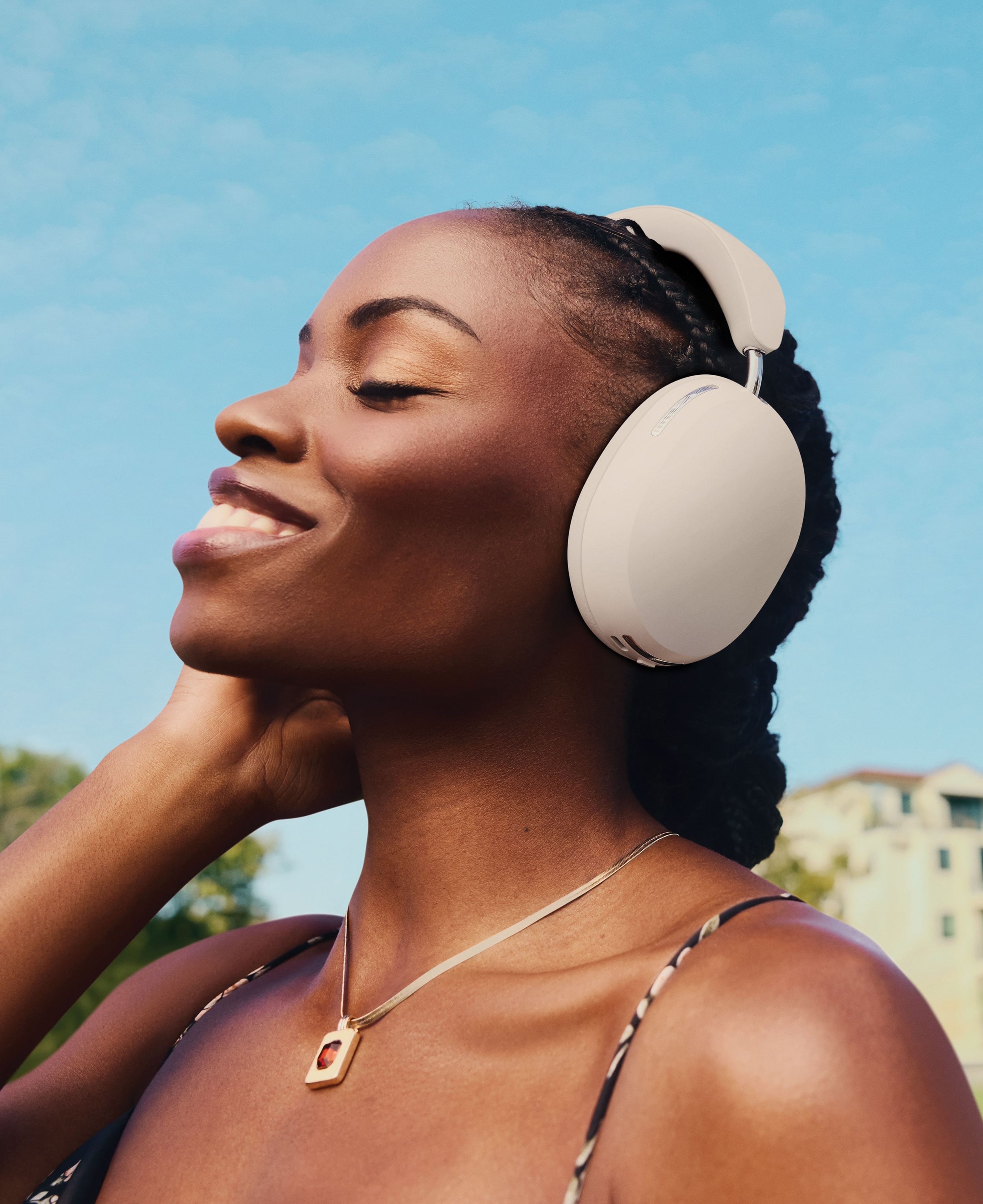 Person, der smiler, lytter til musik på hvide Sonos Ace-hovedtelefoner, mens han går i parken