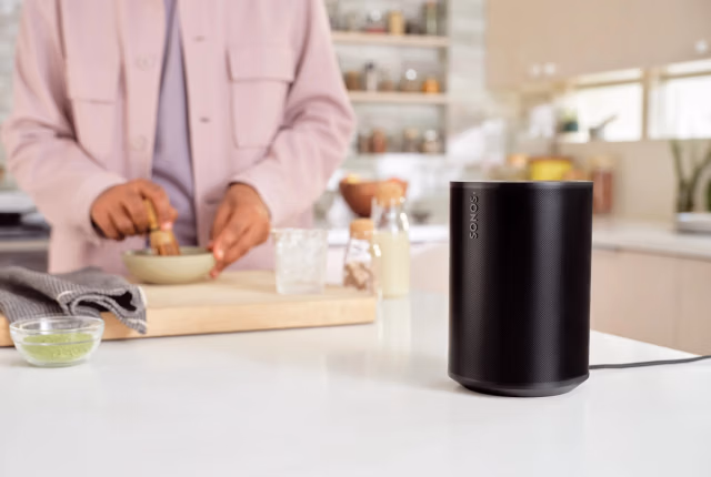 A black Era 100 speaker on a kitchen countertop next to someone preparing a drink