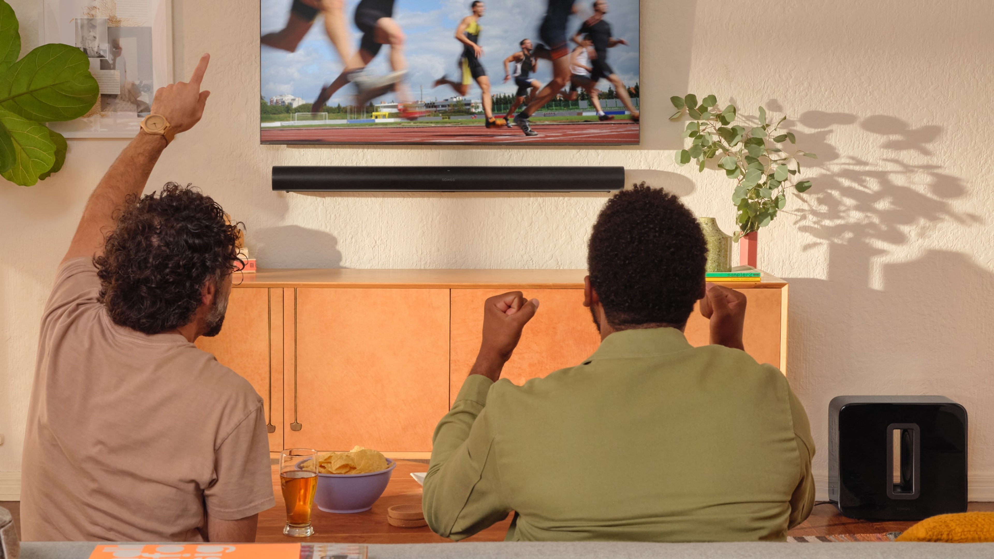 Twee mensen die naar atletiek kijken op een tv met een zwarte Arc en Sub