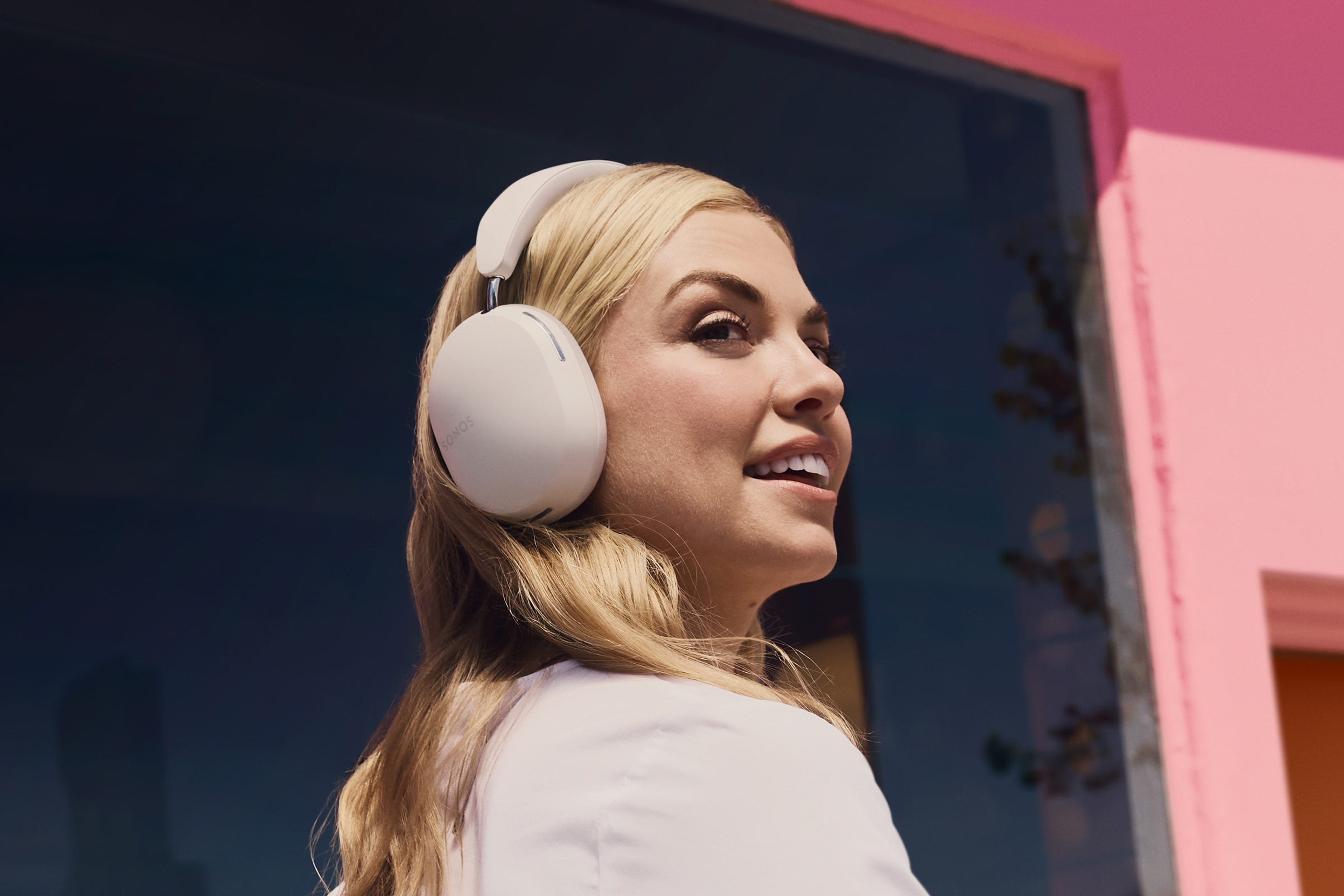 Person smiling wearing Sonos Ace in white next to a pink wall