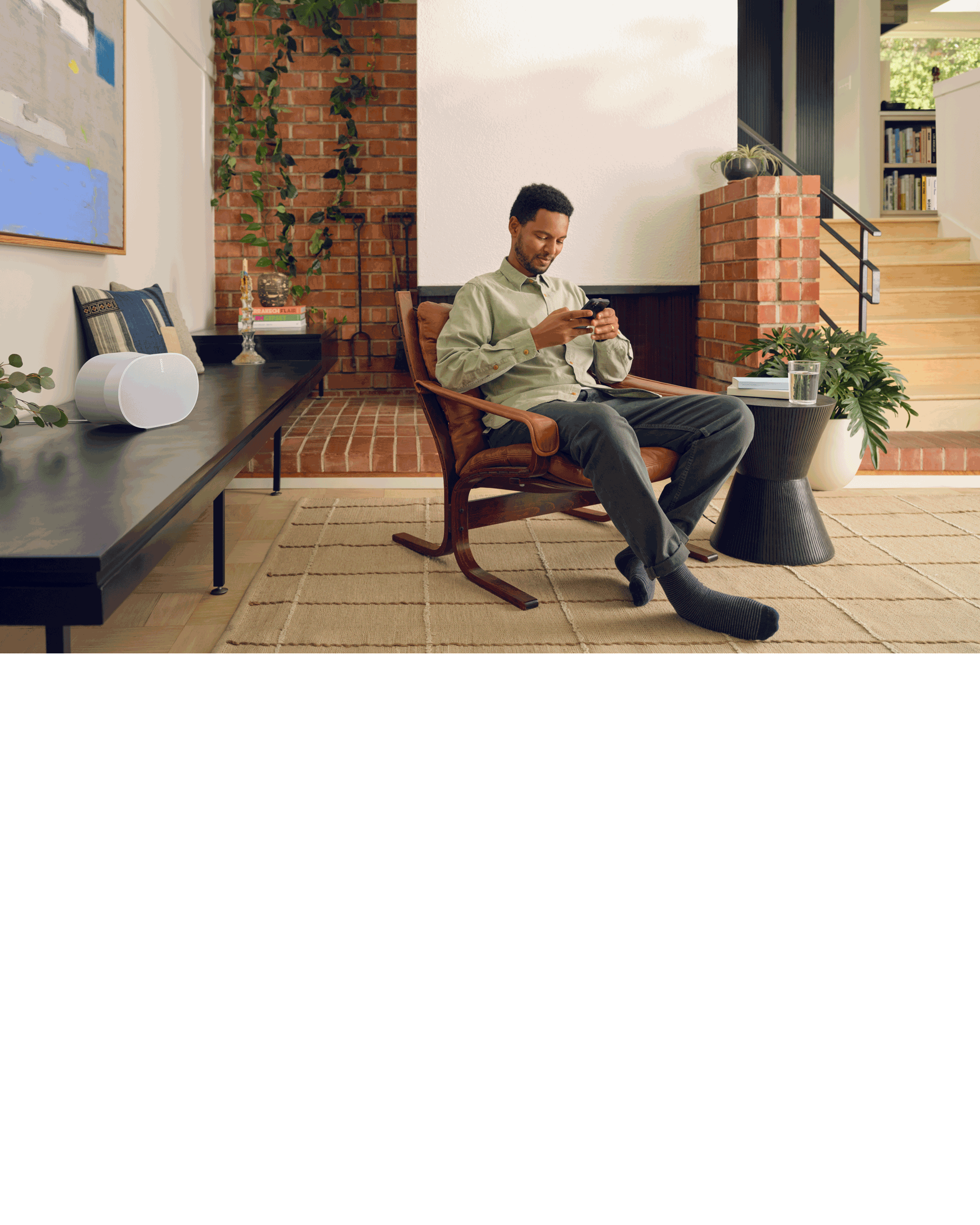 Un utilisateur assis dans un fauteuil contrôlant une enceinte Sonos Era 300 blanche avec l'application Sonos