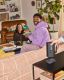 A group of friends gathered in the living room over pizza while one places a black Sonos Play portable speaker on its charging base