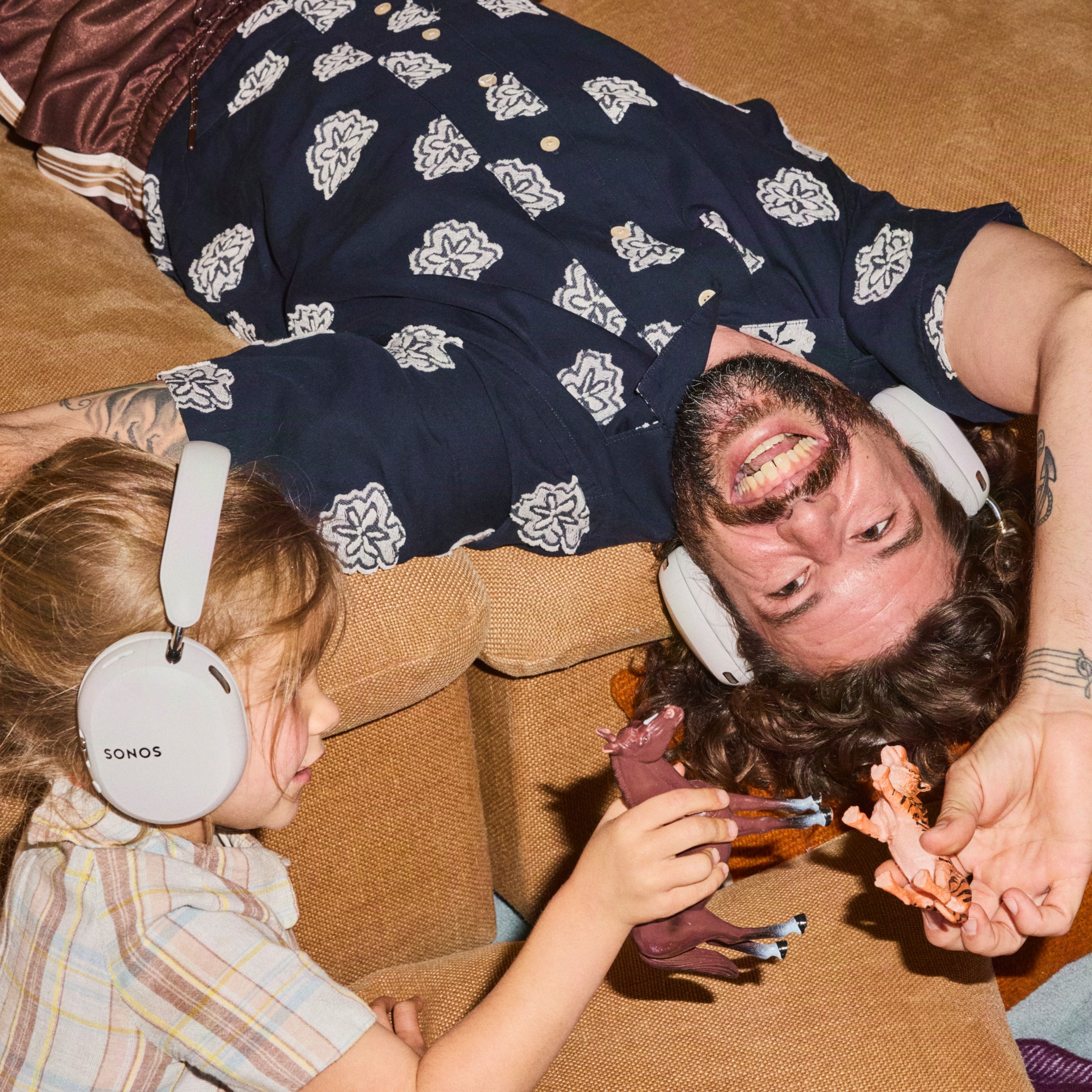Father and daughter playing together on the couch while wearing Sonos Ace Ultra headphones in Sand