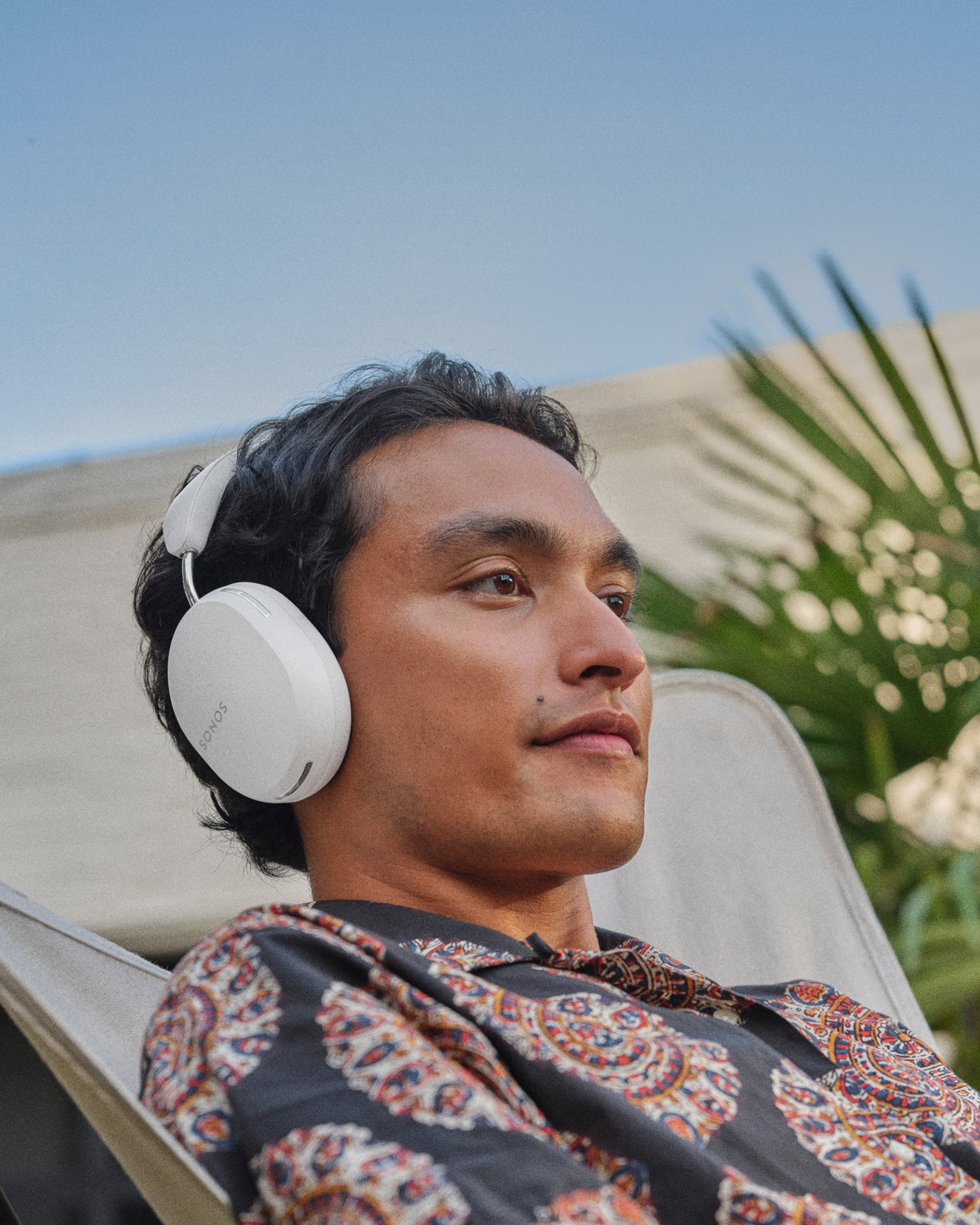 Person listening to music on a white Sonos Ace headphones outdoors