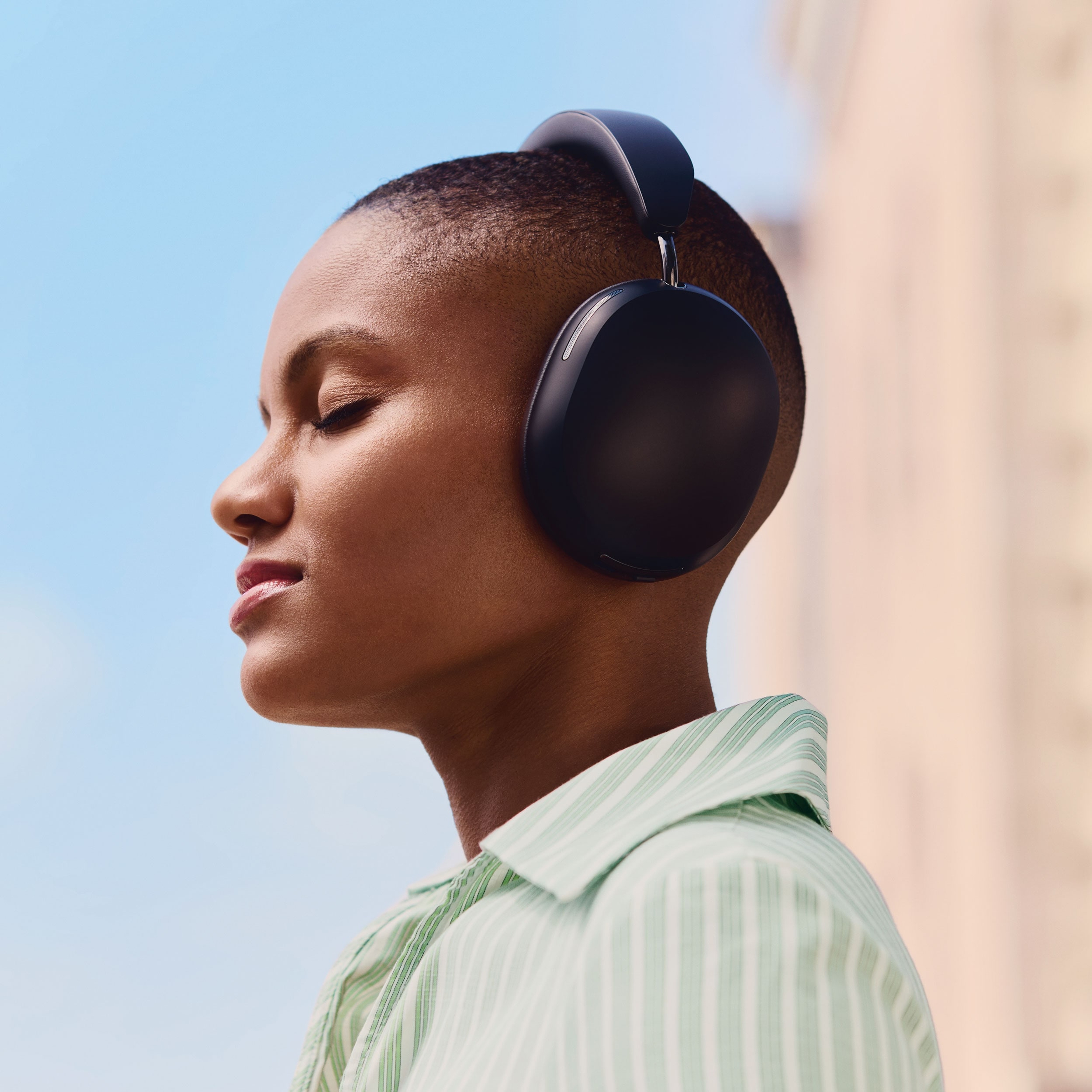 Male user wearing a pair of black Sonos Ace headphones while seated in a chair