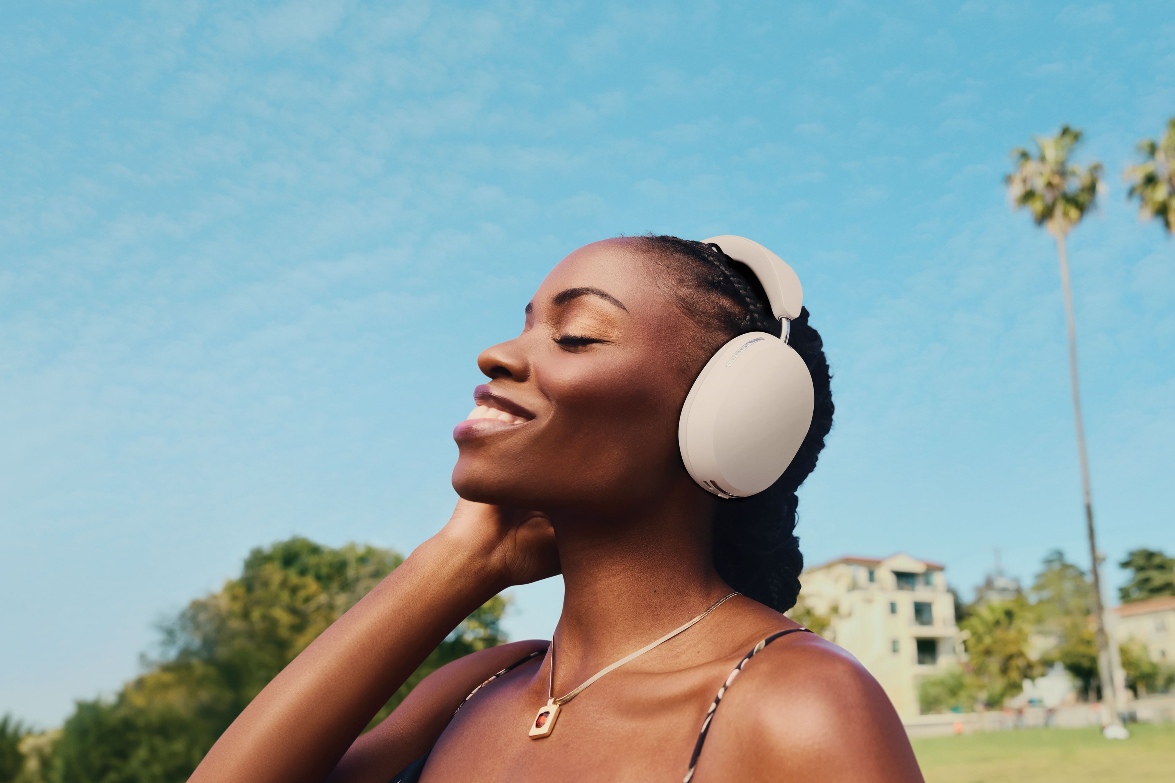 Una persona sonríe y escucha música en sus audífonos Sonos Ace en color soft white mientras camina por el parque